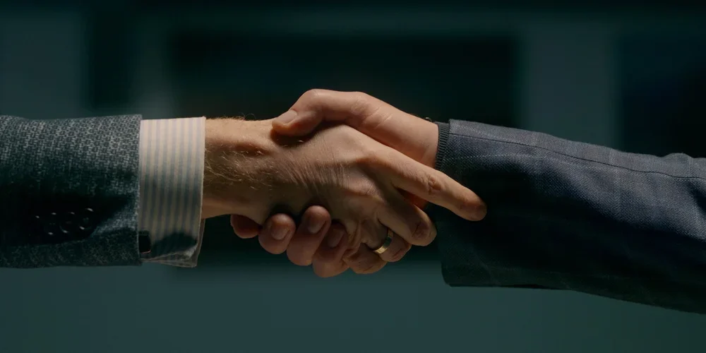Close-up of two people in business suits shaking hands.
