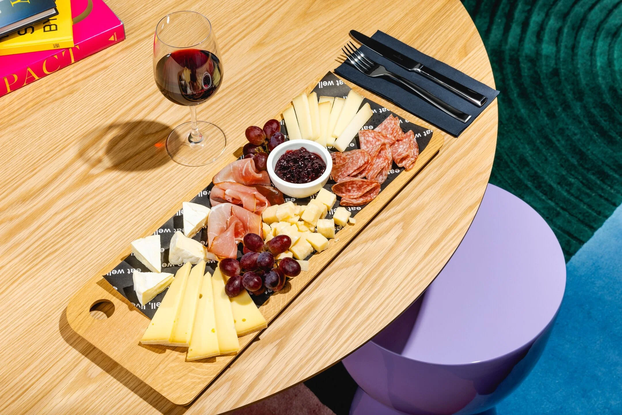 Cheese, grapes, and charcuterie on a wooden serving board with a glass of red wine.