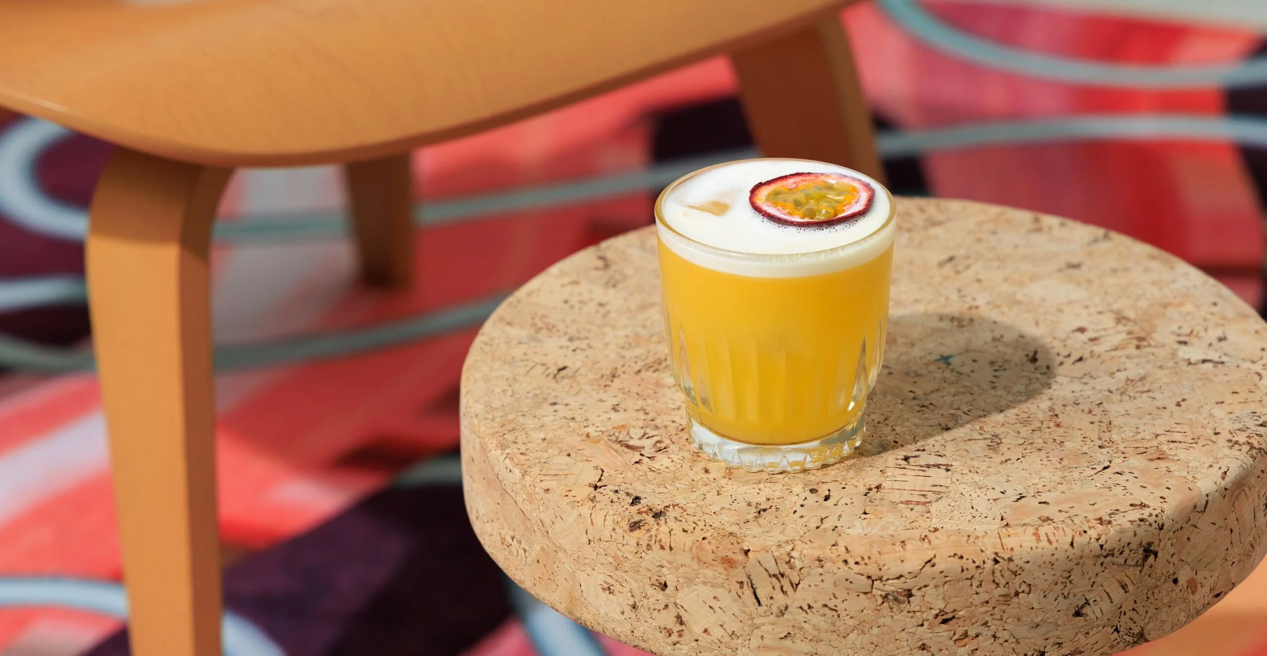 A glass of passion fruit juice topped with passion fruit seeds on a small round wooden table.