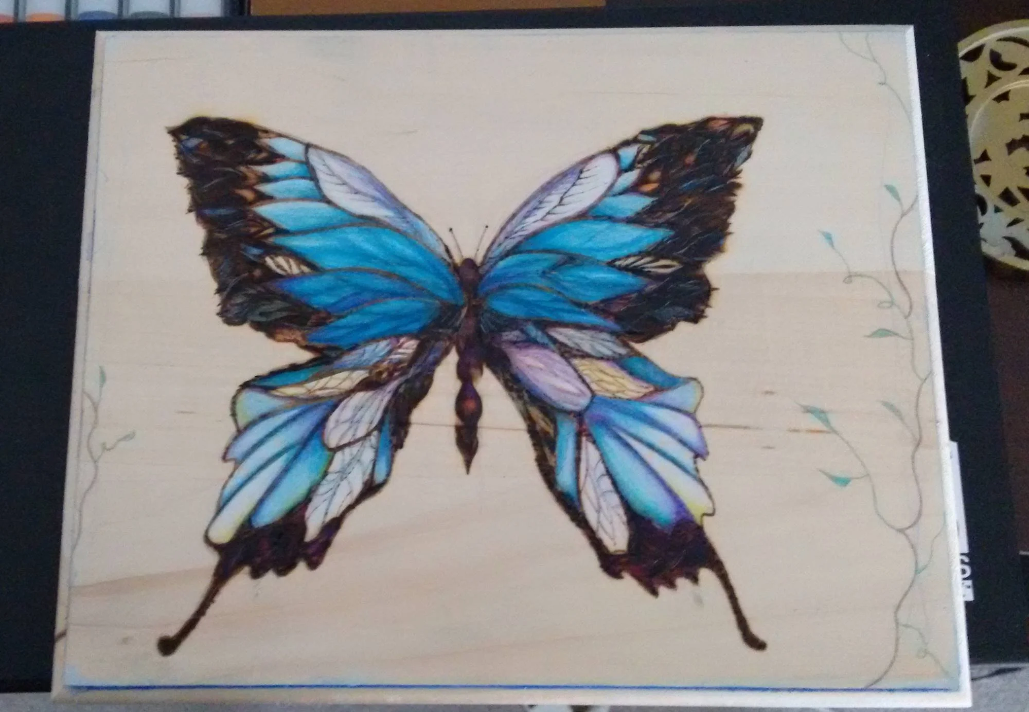A colorful butterfly illustration burned into a wooden panel with blue, purple, yellow, and black details.