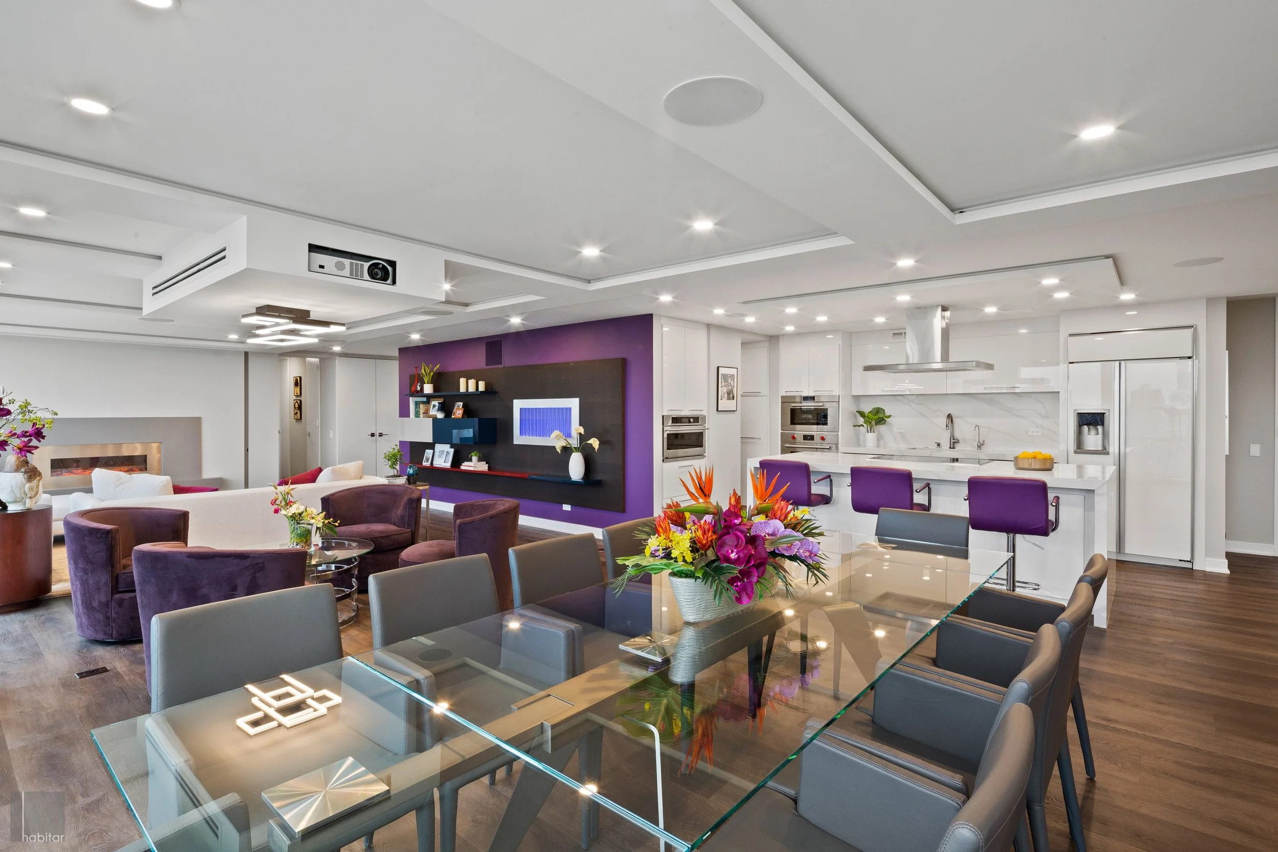 Spacious modern living room and kitchen with purple accents, floral arrangements, and seating area.
