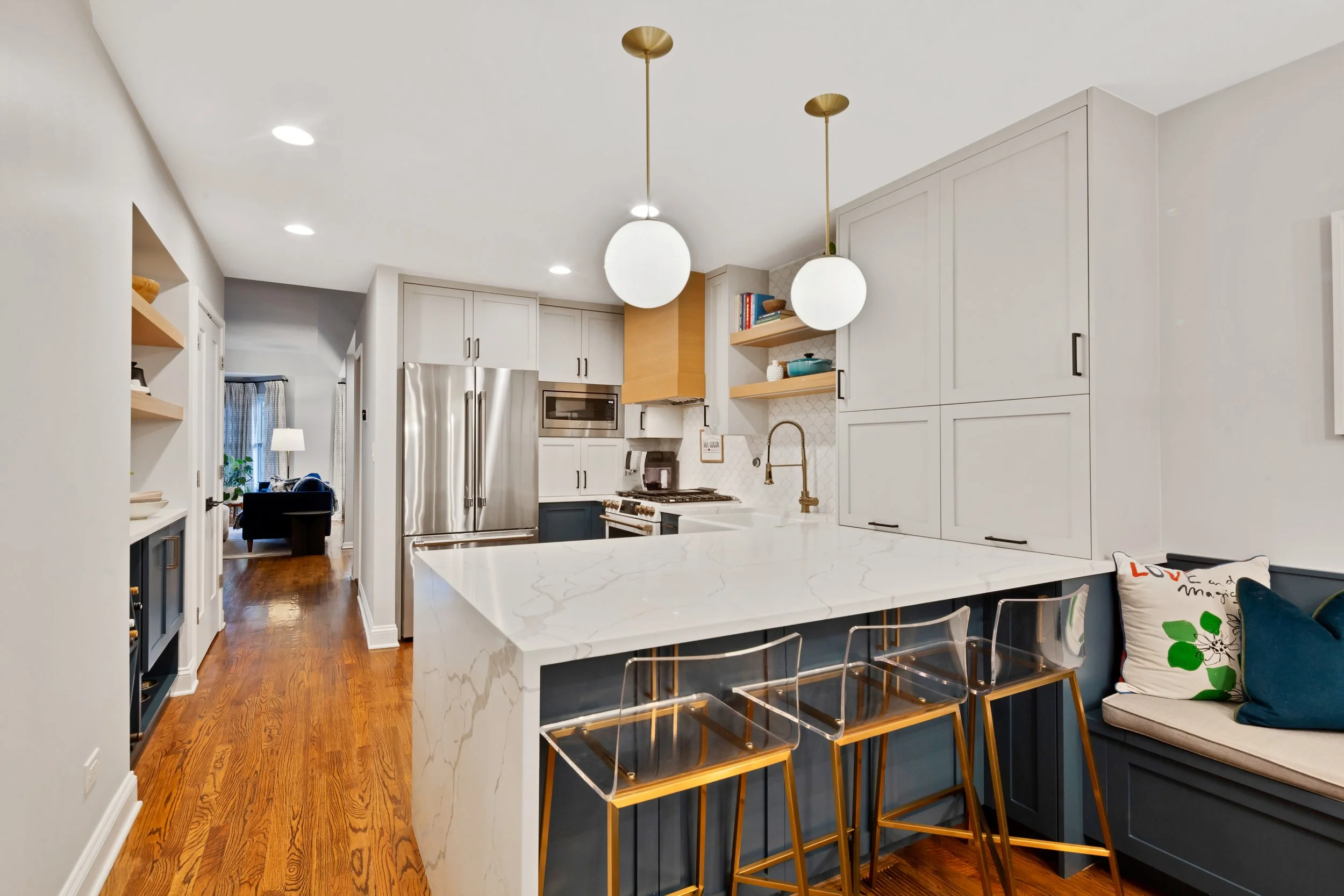 Modern kitchen with white cabinetry, gold pendant lights, marble island, stainless steel appliances, and hardwood floors.