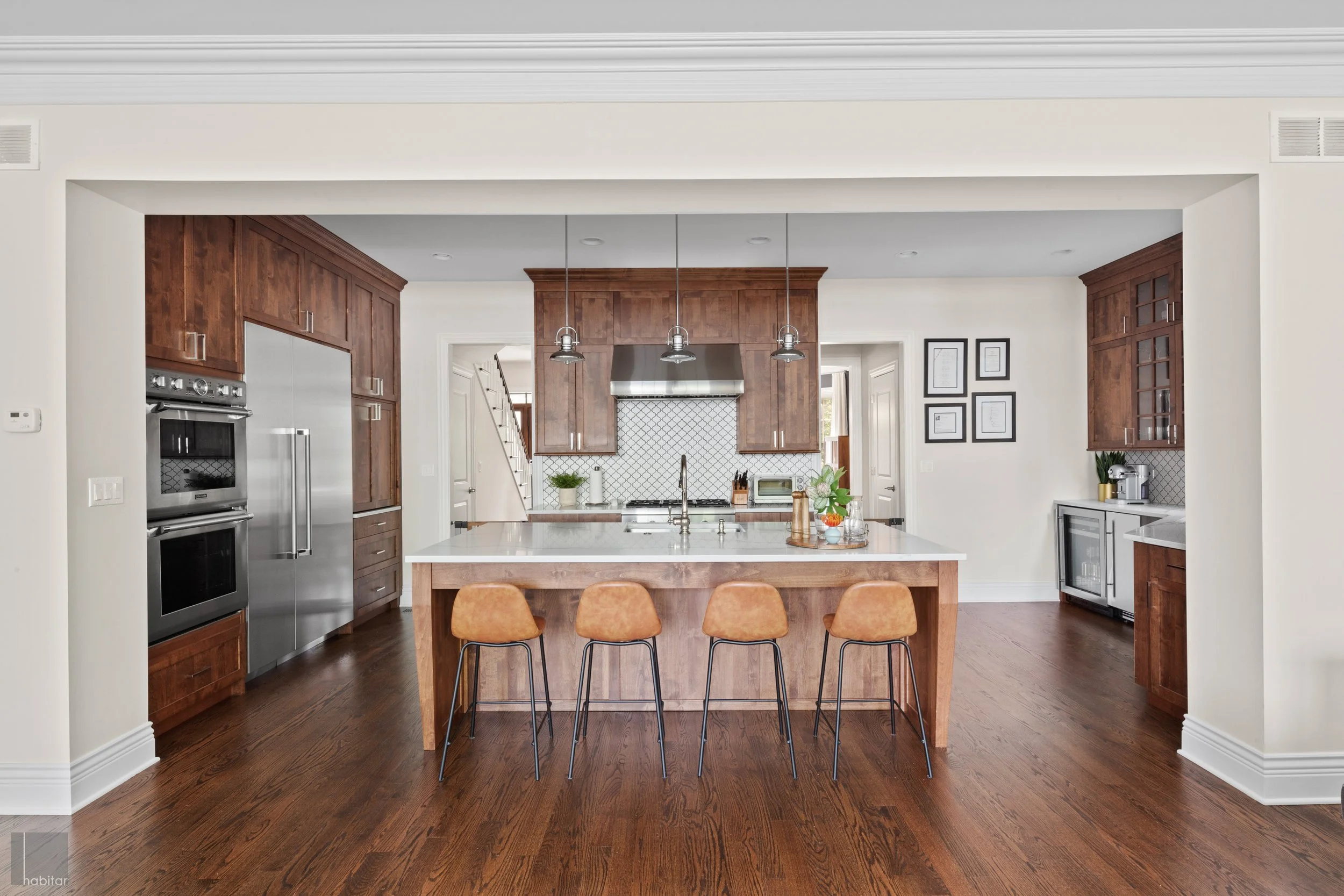 Modern kitchen with wooden cabinets, stainless steel appliances, a central island with four bar stools, and hardwood floors.