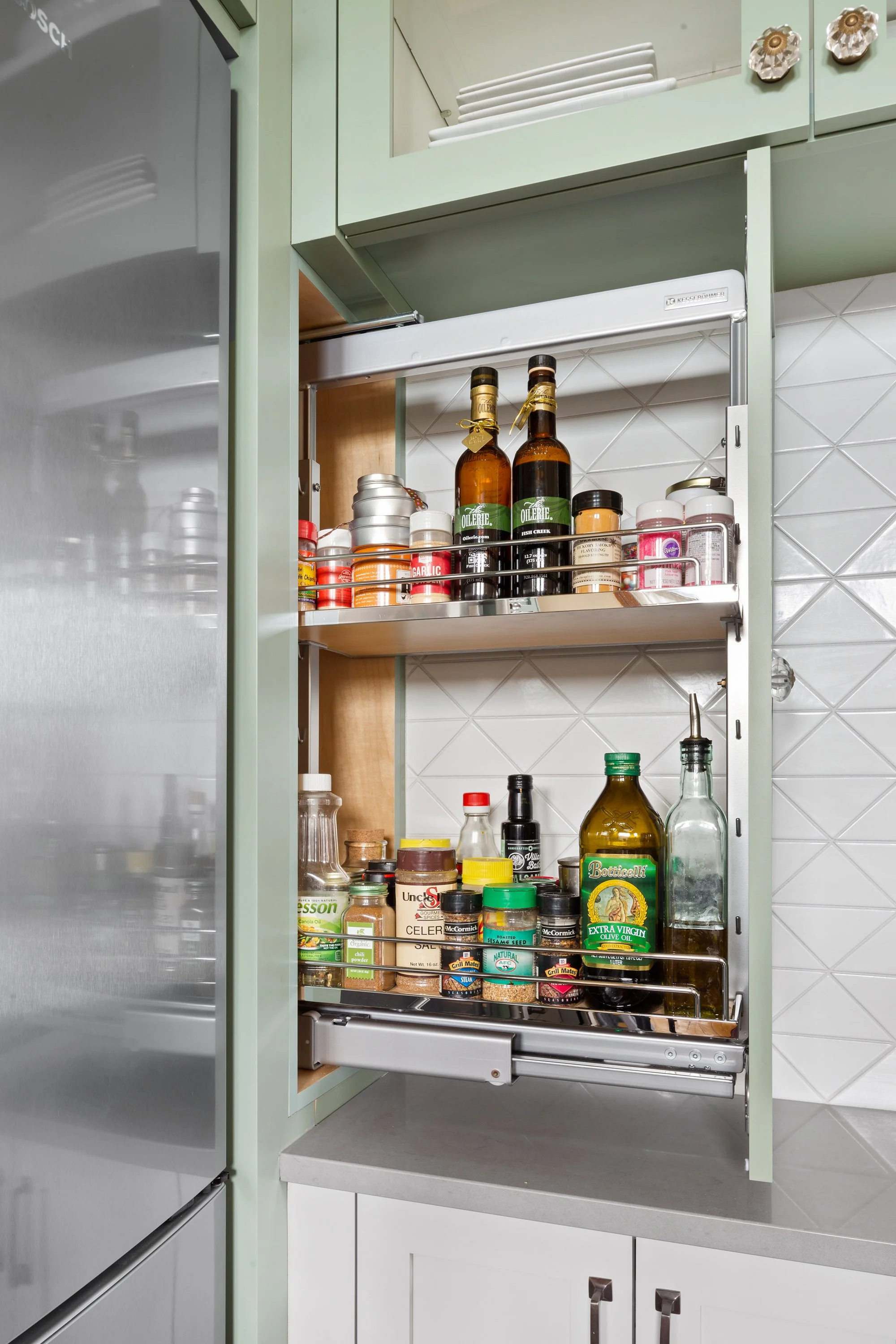 Open pull-out spice and condiment cabinet in a kitchen with various jars, bottles, and spice containers inside.