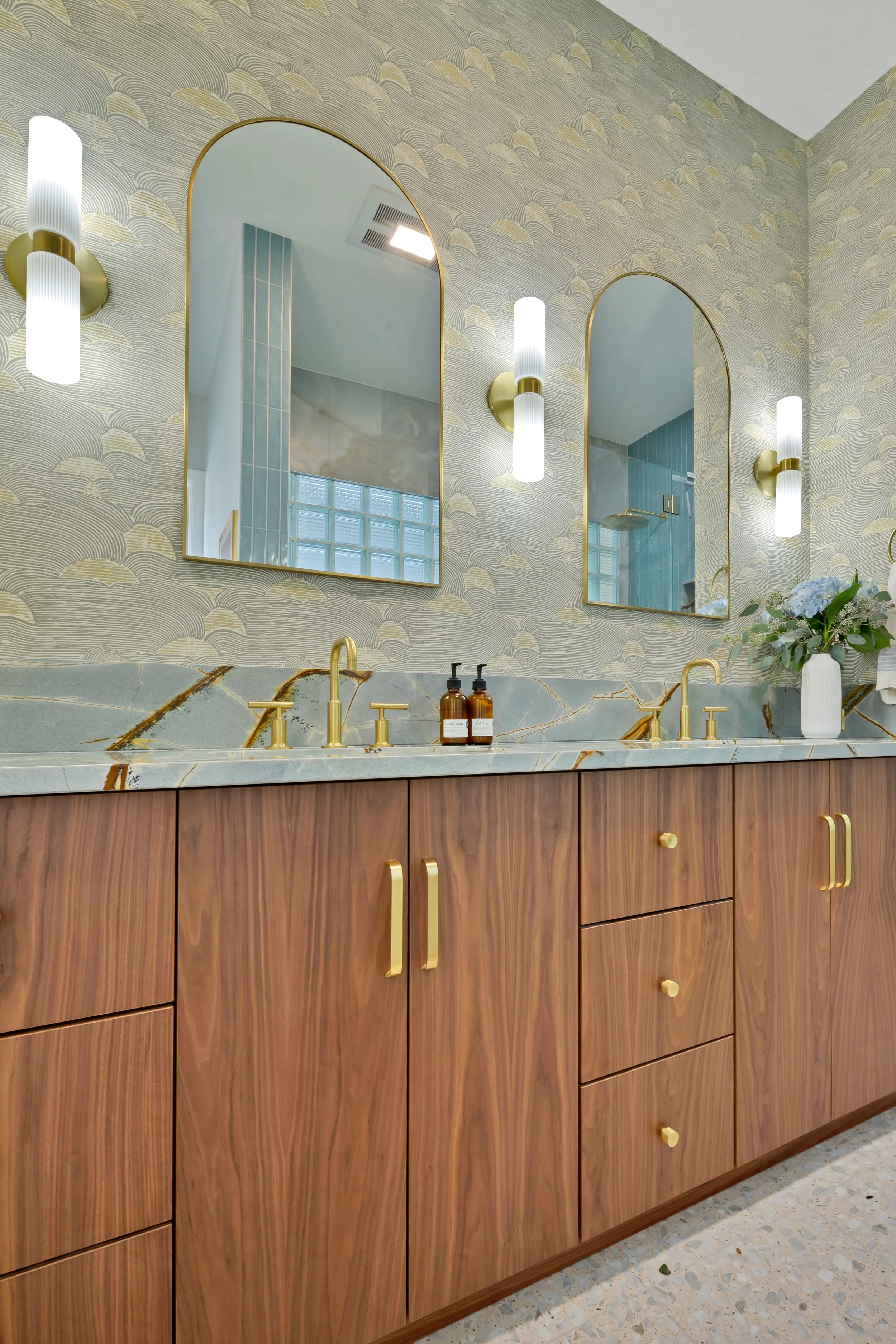 Modern bathroom vanity with wood cabinet, marble countertop, gold fixtures, dual sinks, and mirrors with wall sconces.