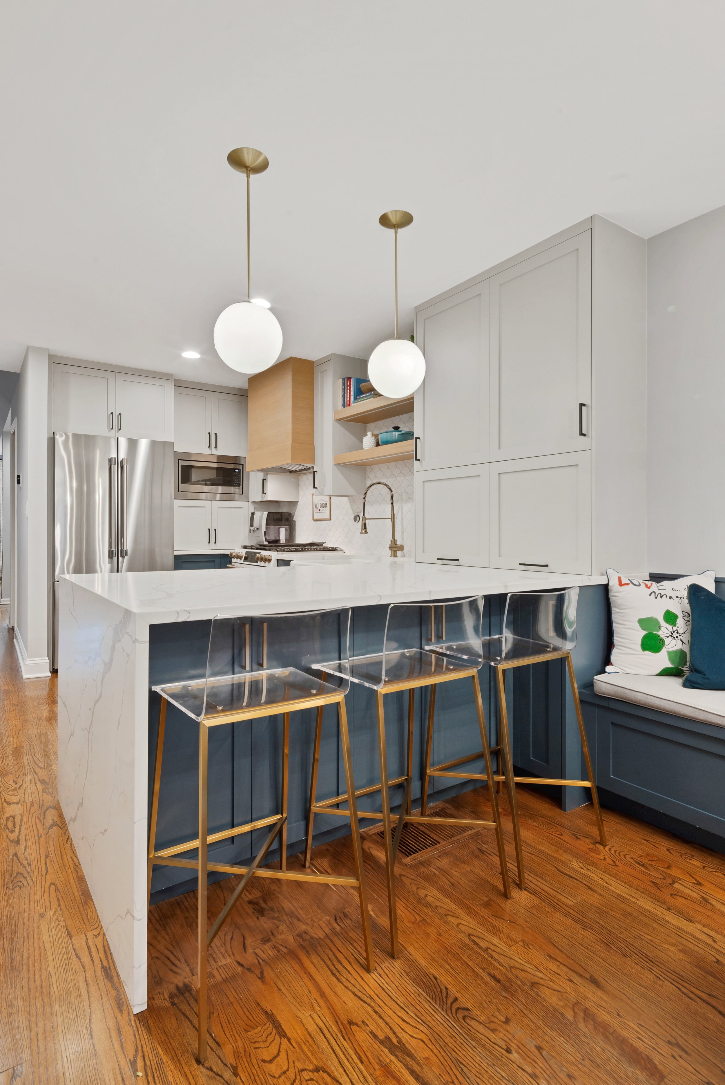 Modern kitchen with white cabinets, stainless steel appliances, a marble island, and three gold and clear acrylic chairs.