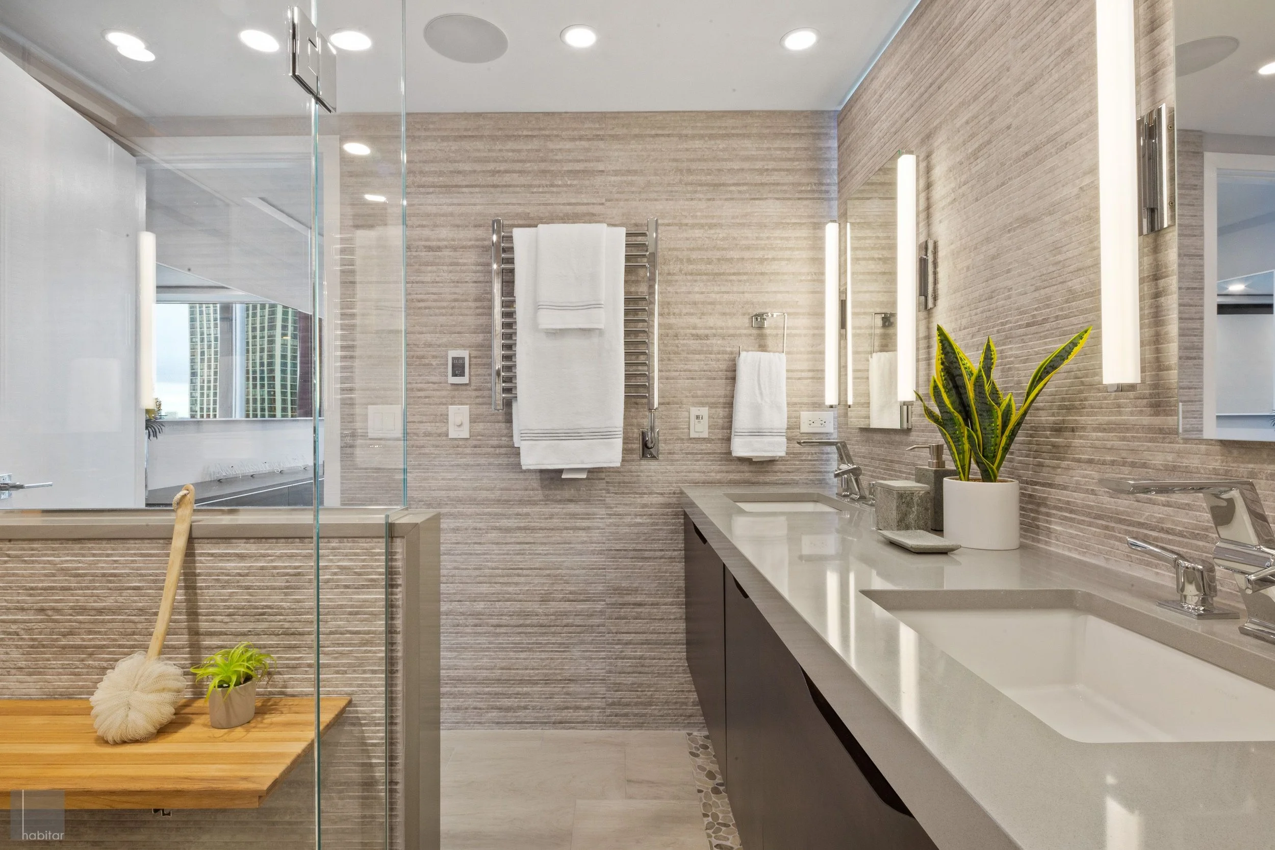 Modern bathroom with double sinks, large mirror, potted plant, and towels on wall-mounted heated towel bars