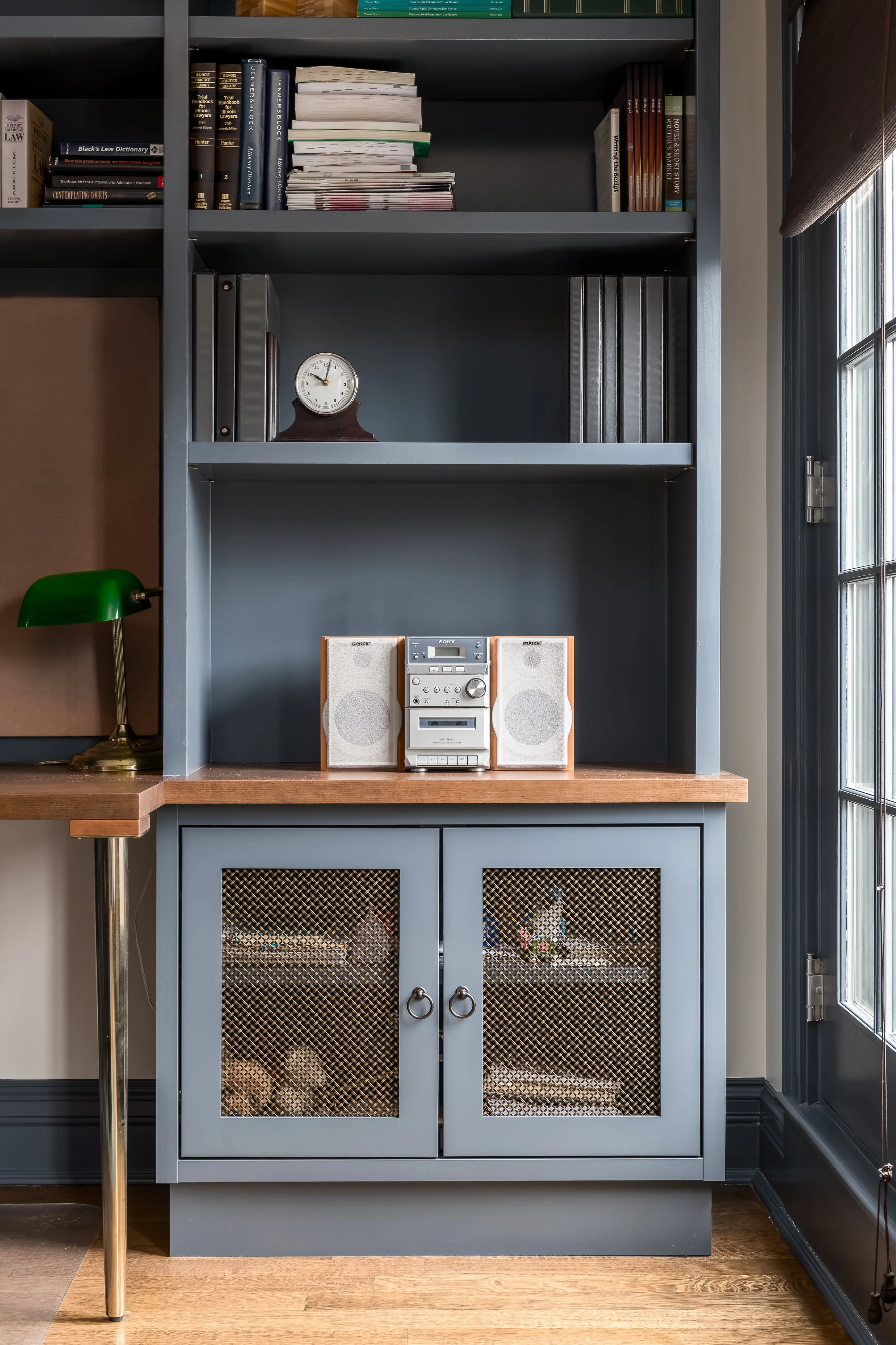 A blue bookshelf with books, binders, and a small clock on the middle shelf, a vintage stereo system with two speakers on a wooden surface, and wicker baskets inside cabinet doors beneath the surface.