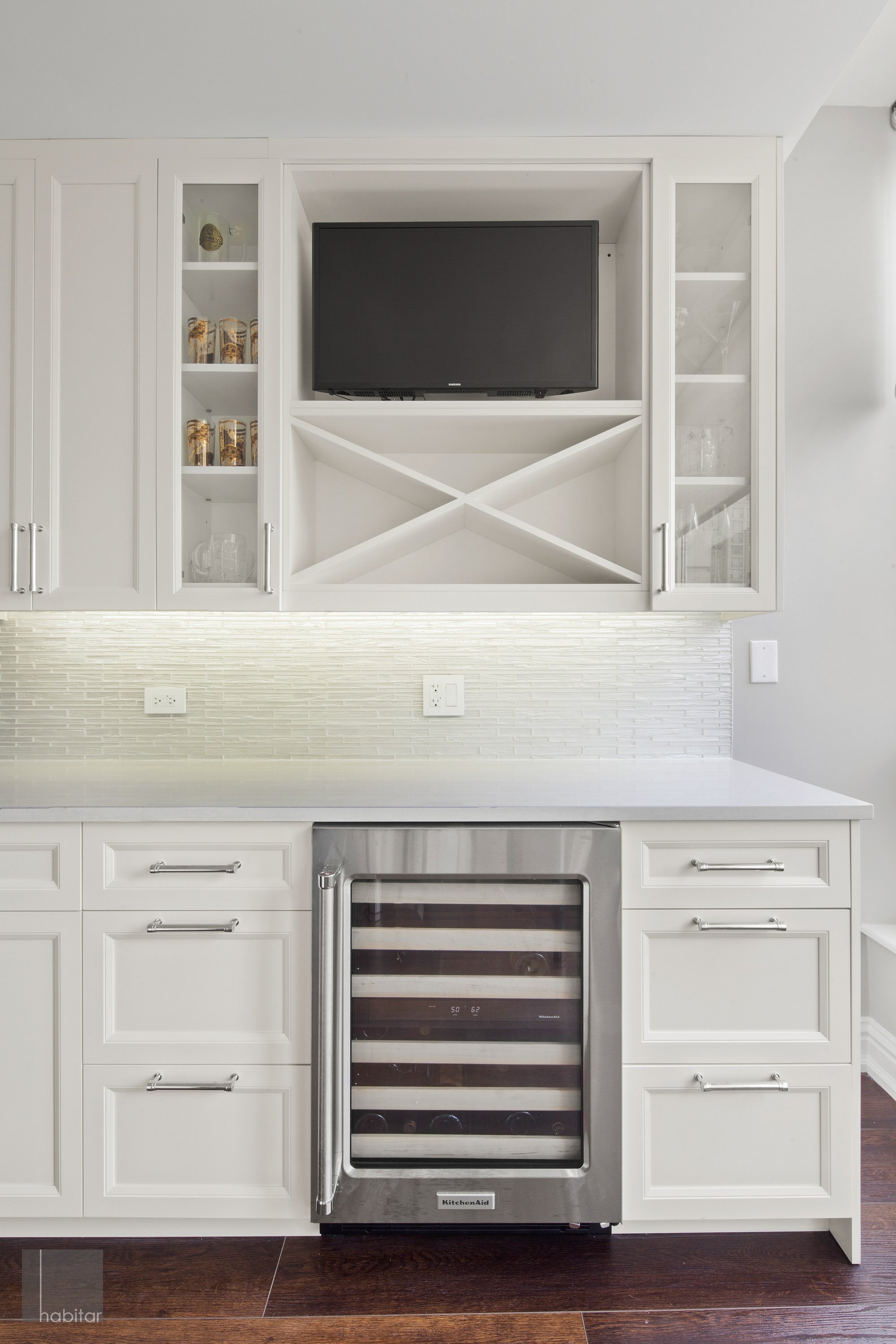 Kitchen with white cabinets, a wine cooler, a small white countertop, and a cabinet with a mounted television.