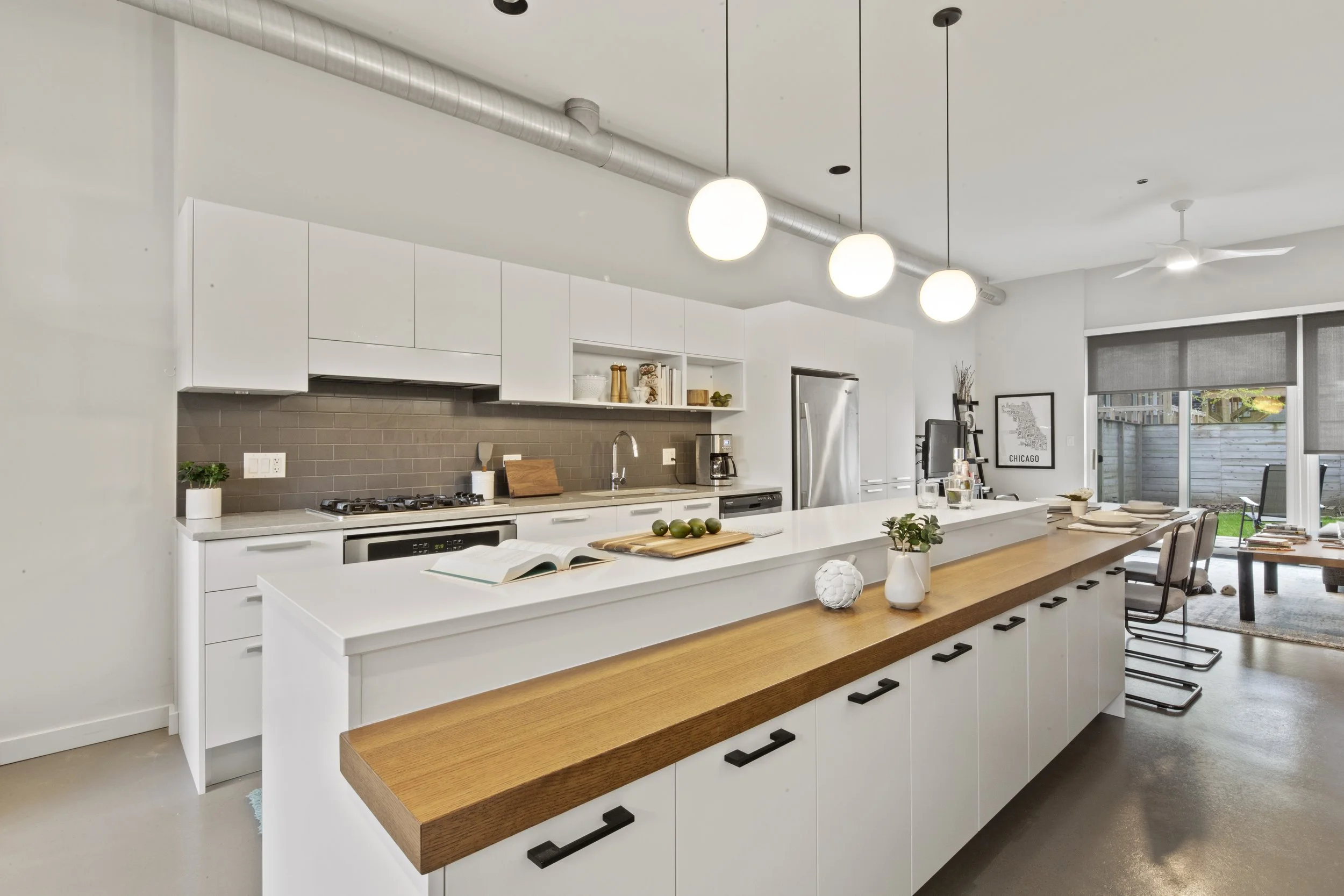 Modern kitchen with white cabinets and a wooden countertop island, featuring a map of Chicago and a dining area with table and chairs in the background.