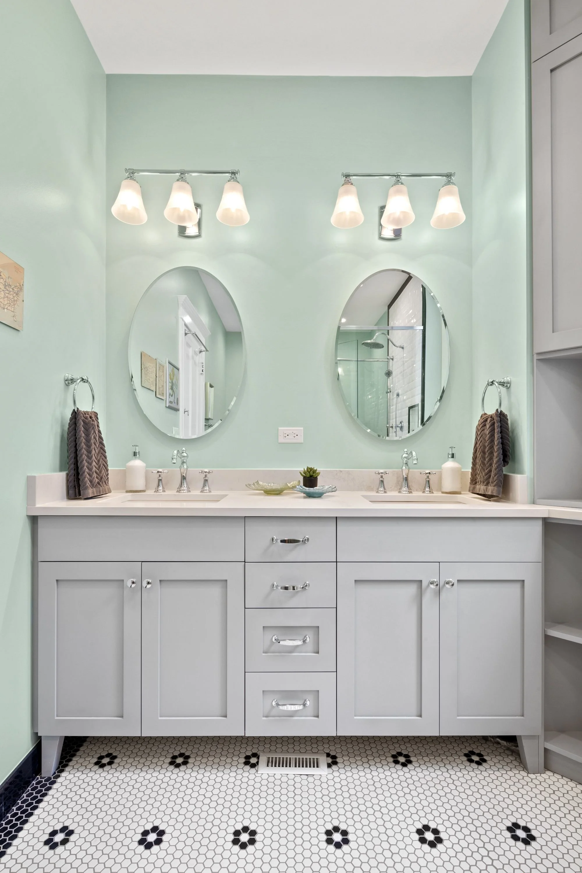 Bathroom with double vanity, round mirrors, white cabinets, and black-and-white hexagon floor tiles.