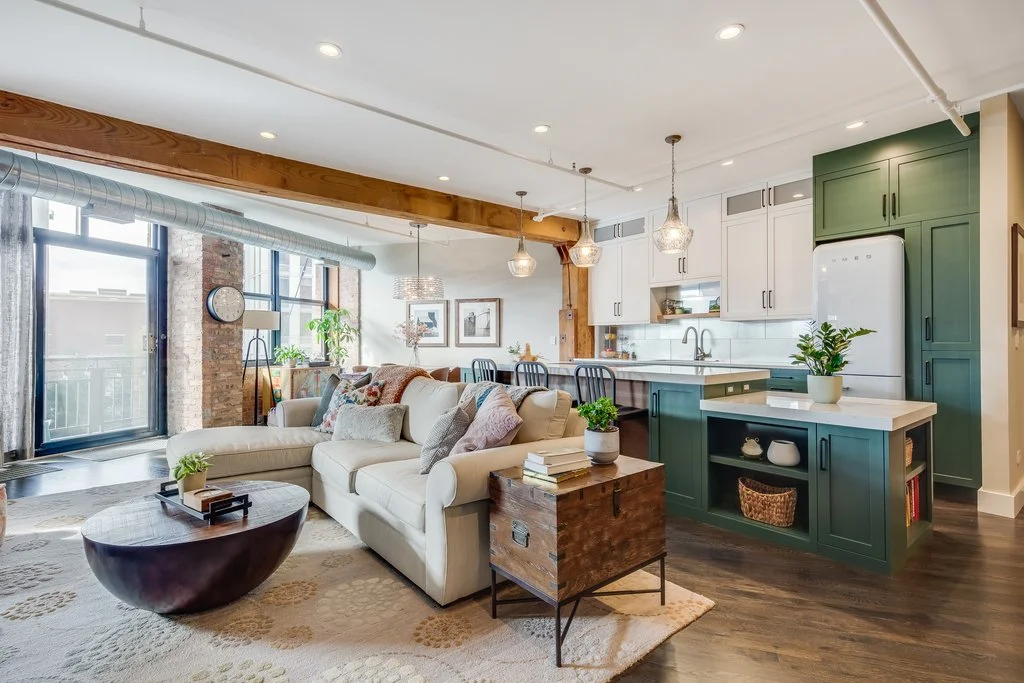 Open concept living room and kitchen with a white sofa, green kitchen cabinets, and large windows letting in natural light.
