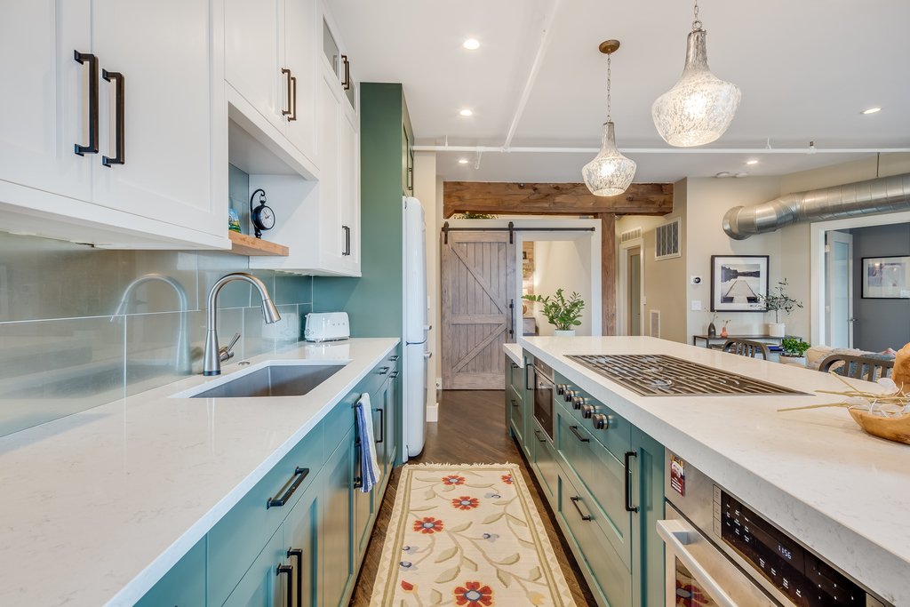 Modern kitchen with white and teal cabinets, a long island with a built-in stove, pendant lights, and a sliding barn door.