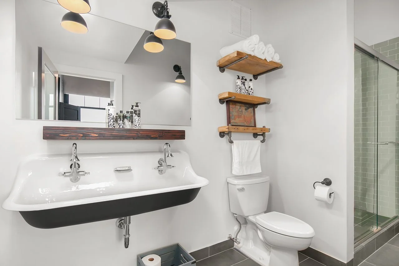 Modern bathroom with a wall-mounted sink, a mirror, hanging shelves above the toilet, and a glass-enclosed shower.