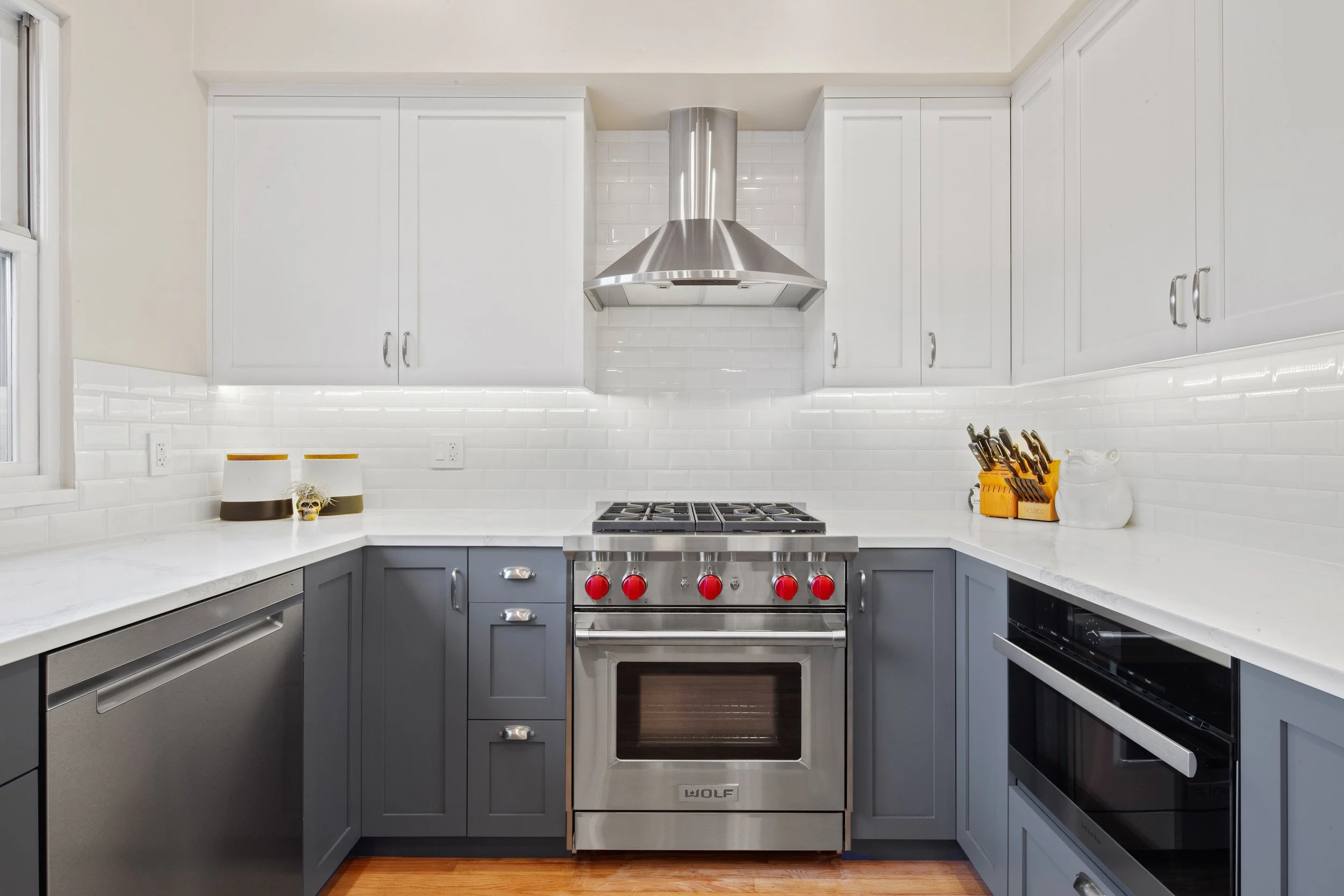Modern kitchen with gray lower cabinets, white upper cabinets, white subway tile backsplash, stainless steel appliances, and a white marble countertop.