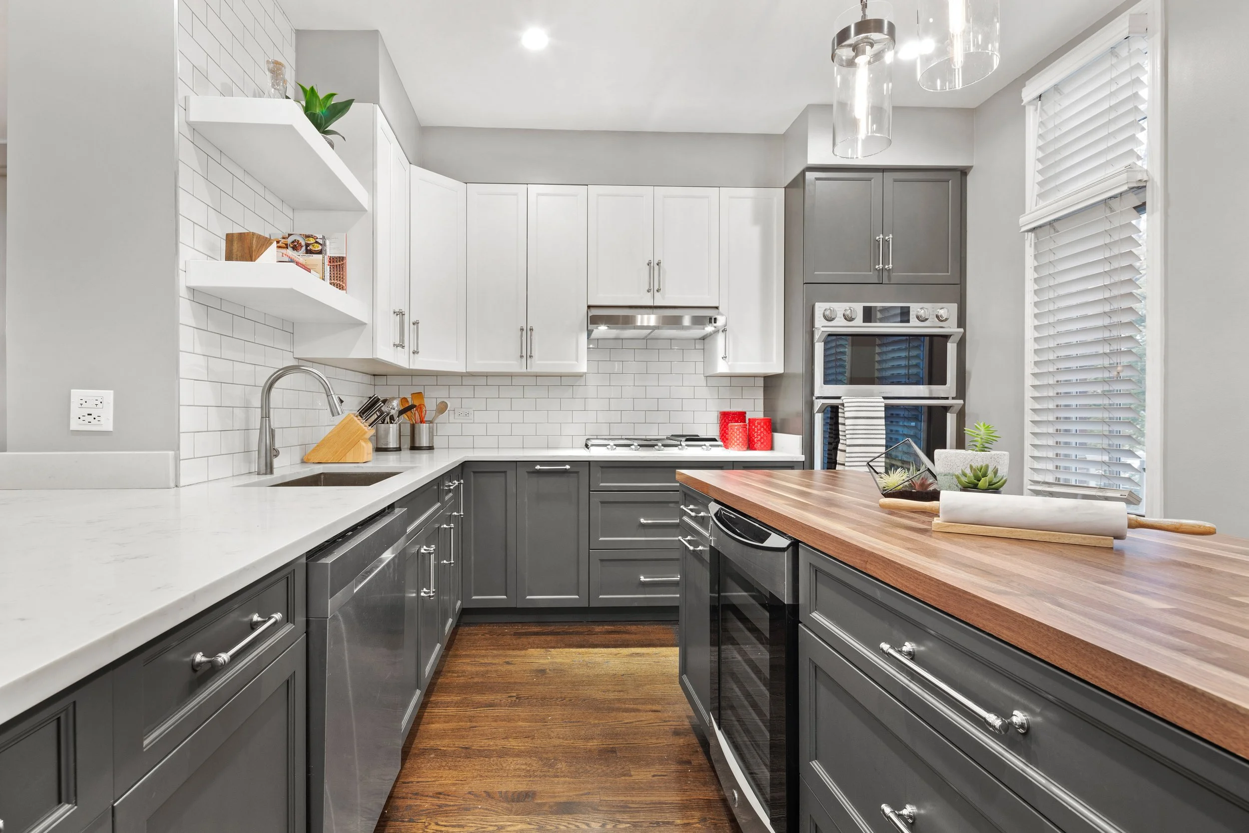 Modern kitchen with gray lower cabinets, white upper cabinets, white subway tile backsplash, stainless steel appliances, and a wooden kitchen island.