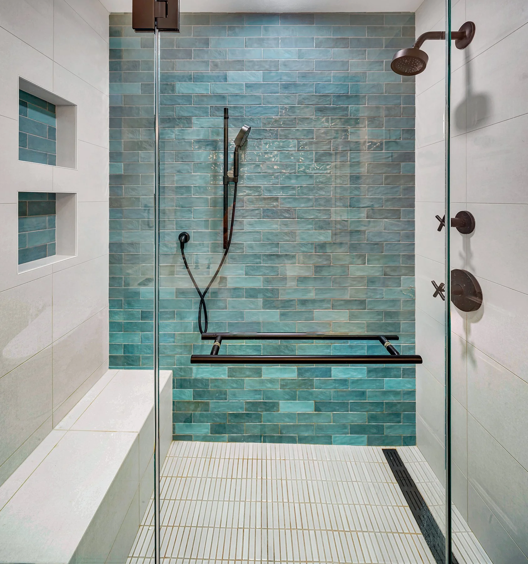 Accessible shower with teal subway tiles, black grab bar, and a built-in tiled bench.