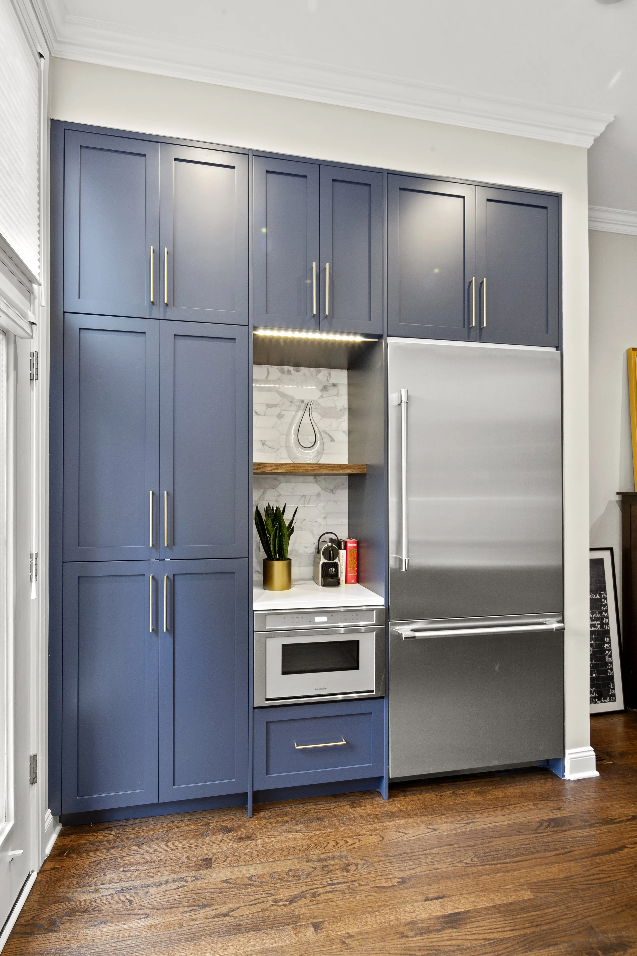 Modern kitchen with blue cabinets, a stainless steel refrigerator, a white marble backsplash, and hardwood floors.