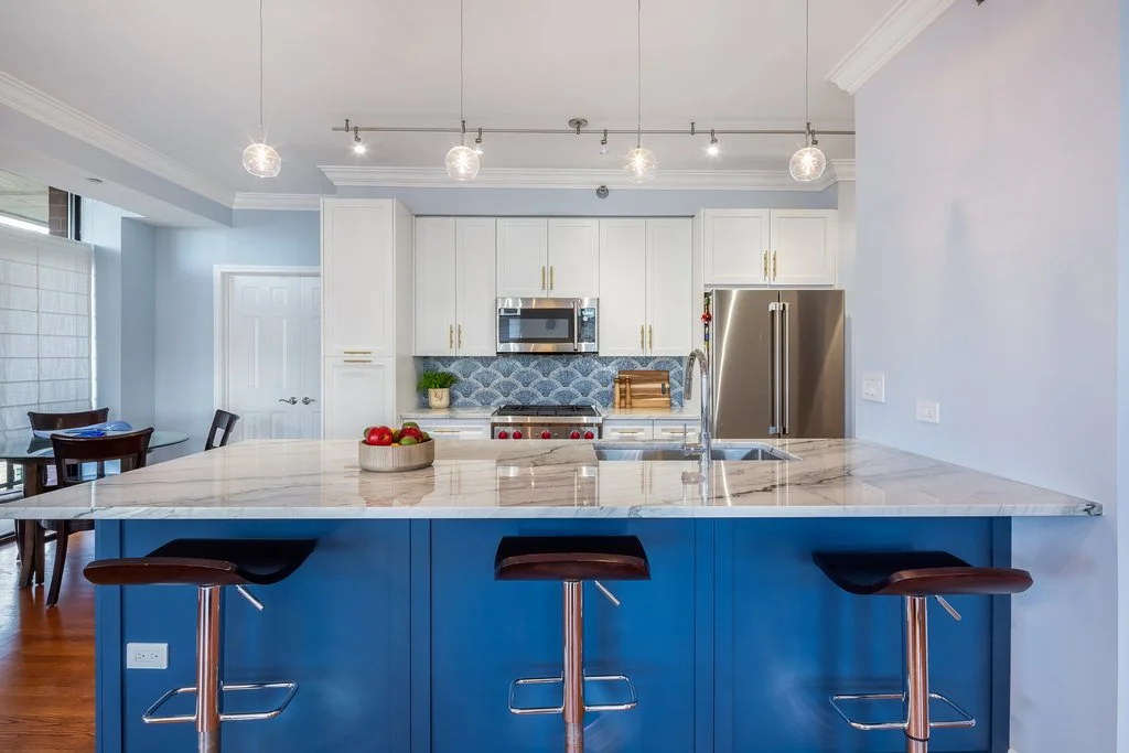 Modern kitchen with white cabinets, marble countertop island with bar stools, stainless steel refrigerator, and decorative backsplash.