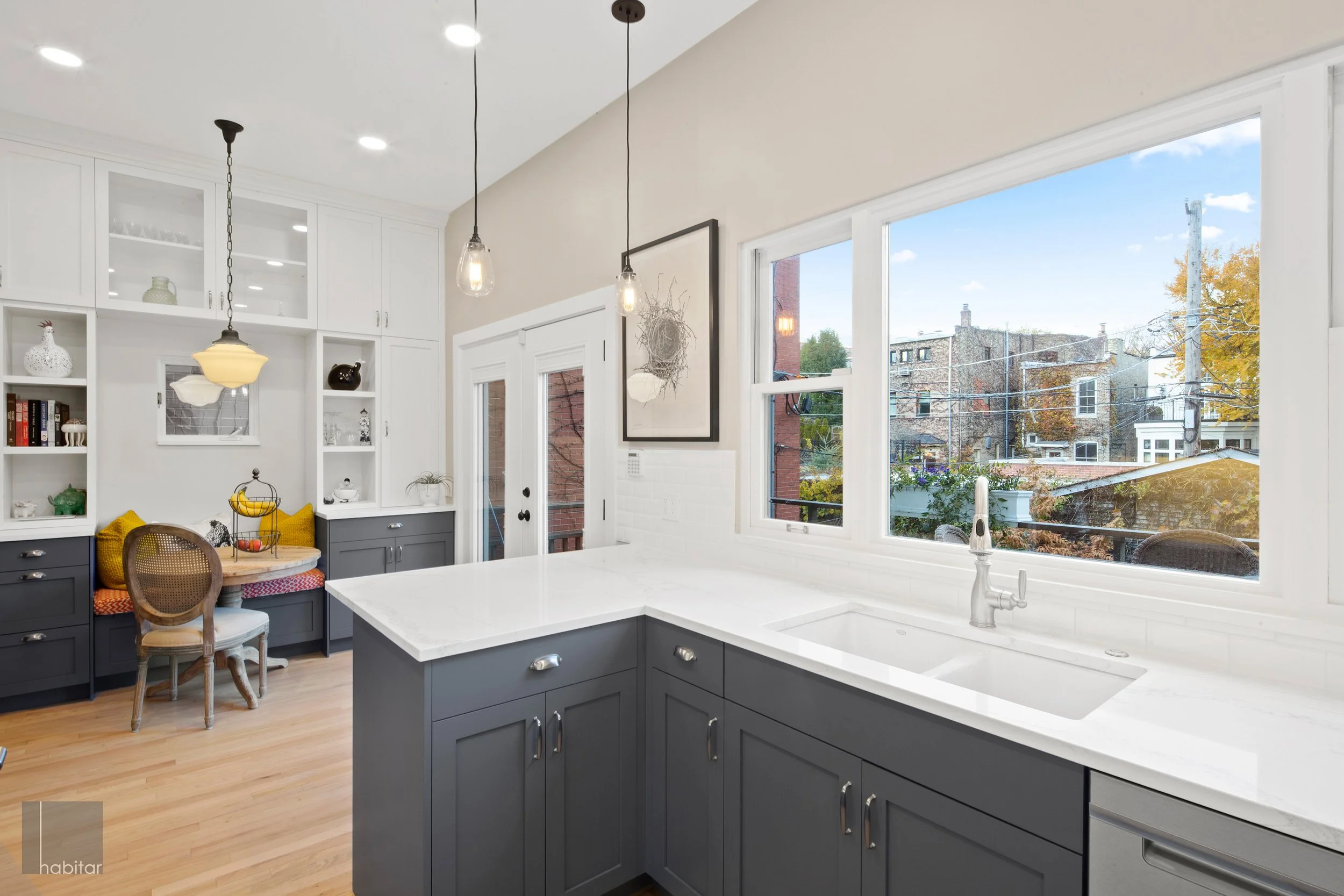 Modern kitchen with gray cabinets, white countertops, large windows, and pendant lights.