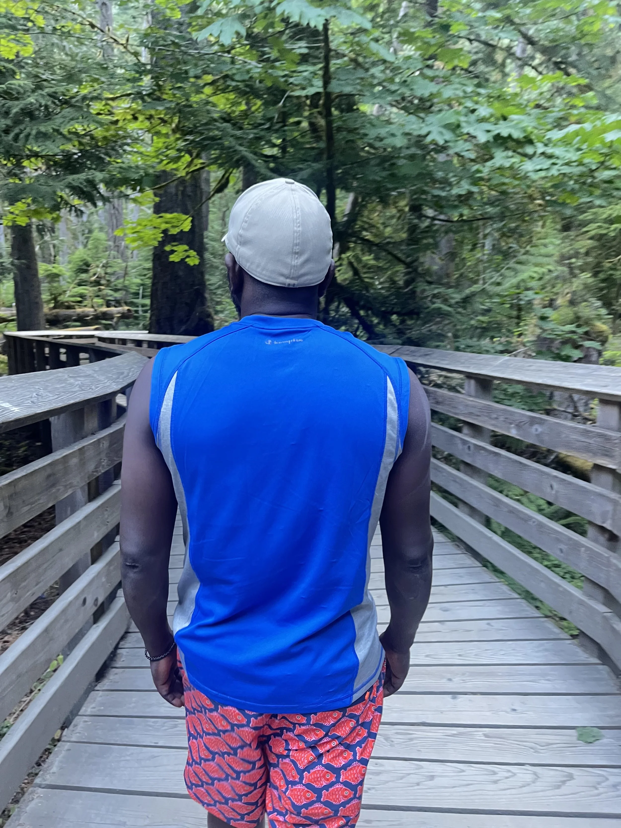 An african man walks with his back to us on wooden bench in the woods of Vancouver Island