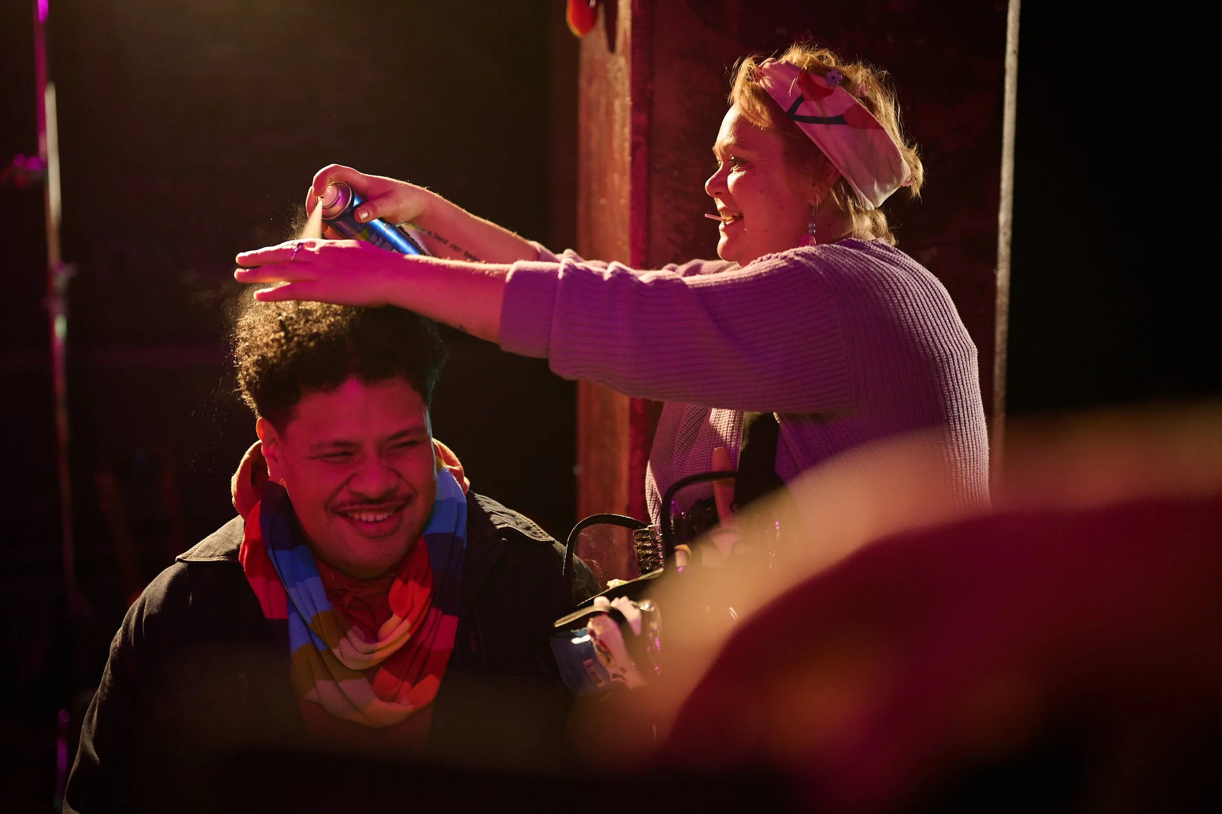 Makeup artist Jim Stanton spraying Actor Albert Latailakepa's hair while filming the Statistics New Zealand commercial 'Data Helps Us Do' in a purple lit up bar