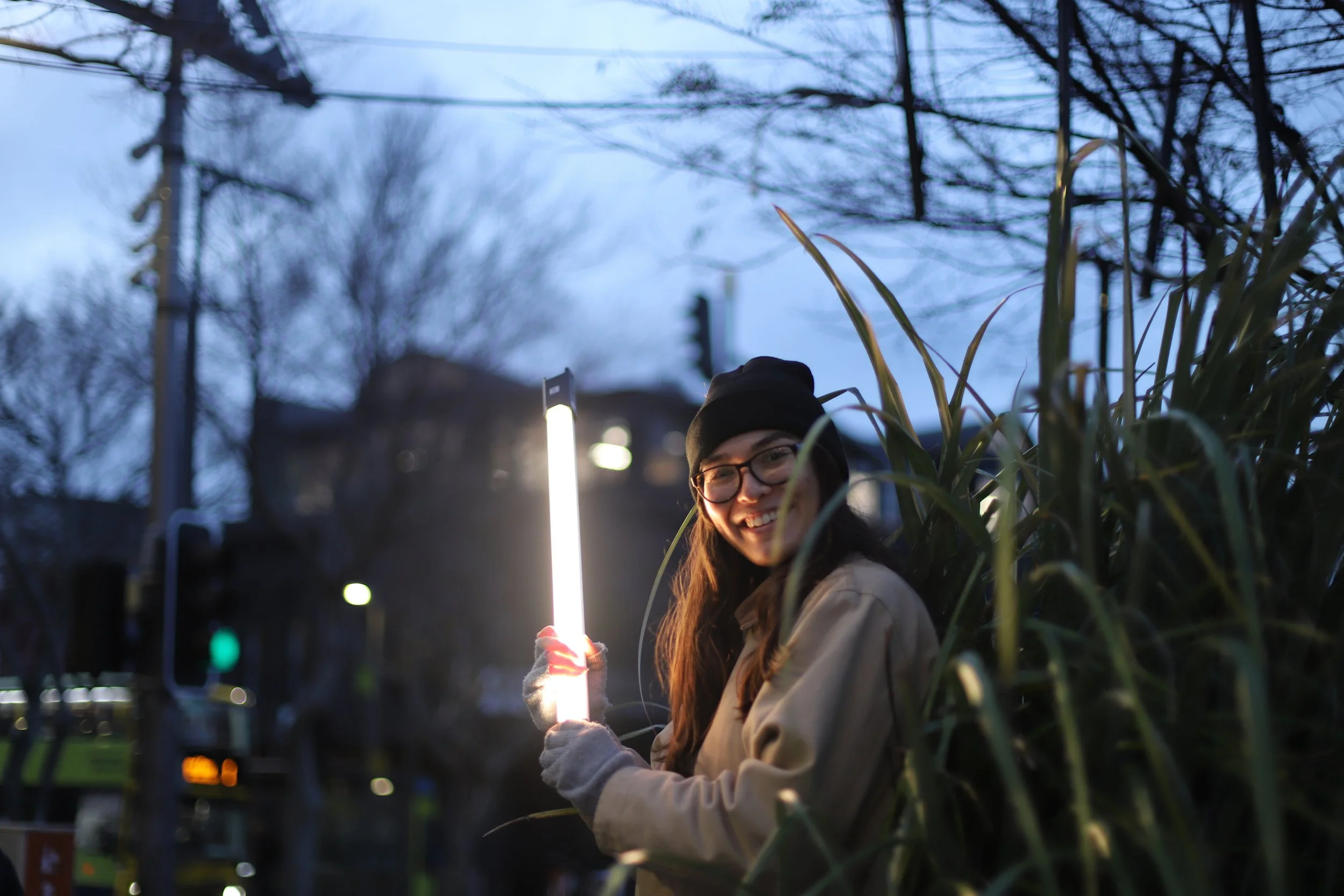 Grace Bush holding a light bar in a flax bush while filming at night
