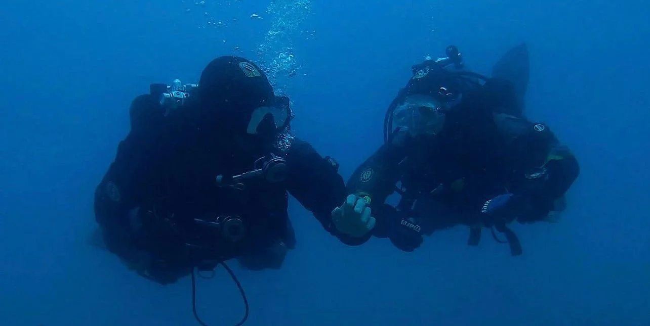Due subacquei in assetto da immersione che si tengono per mano sott'acqua