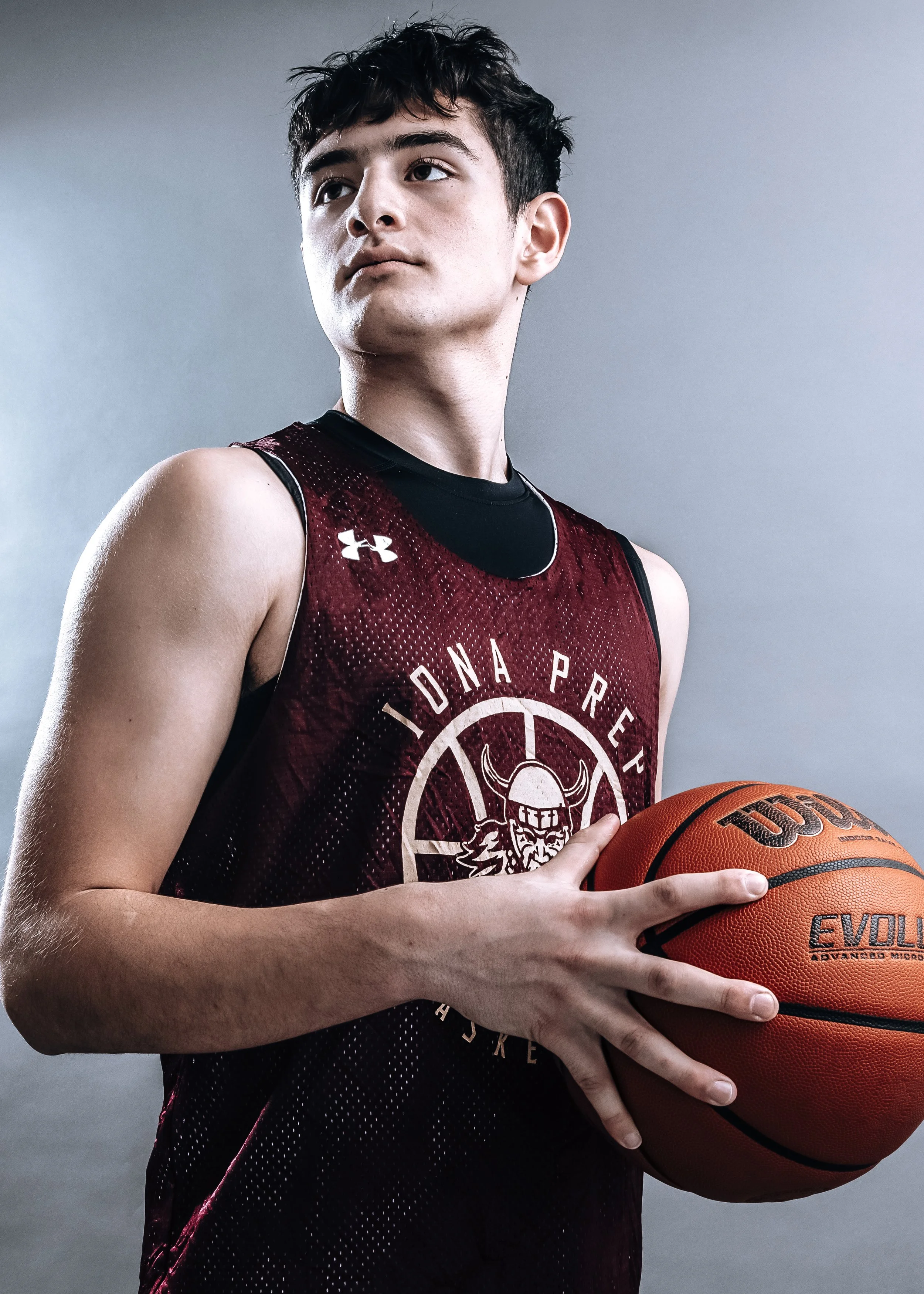 A young male basketball player in a maroon jersey holding a basketball.