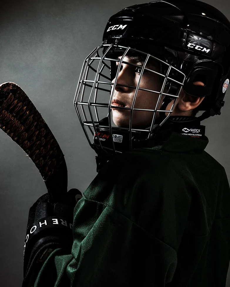 A young ice hockey player wearing a black helmet and green jersey, holding a hockey stick.