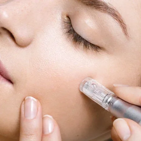 A person applying a skincare product with a rollerball applicator to their cheek.