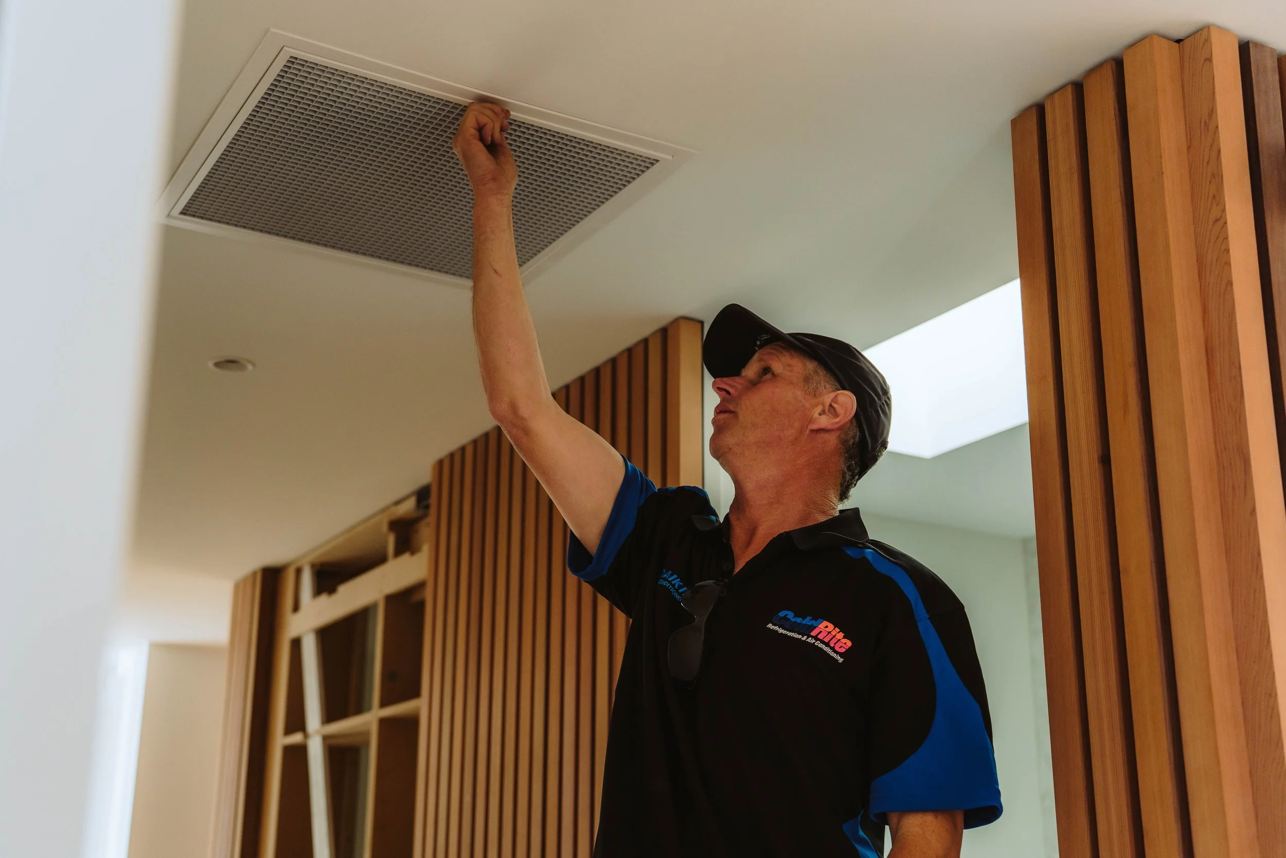 A man installing or inspecting a ceiling vent in a modern interior with wooden accents.