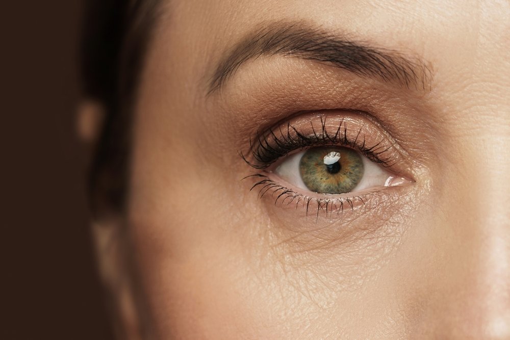Close-up of a woman's eye with green iris, detailed eyelashes, and eyebrows.