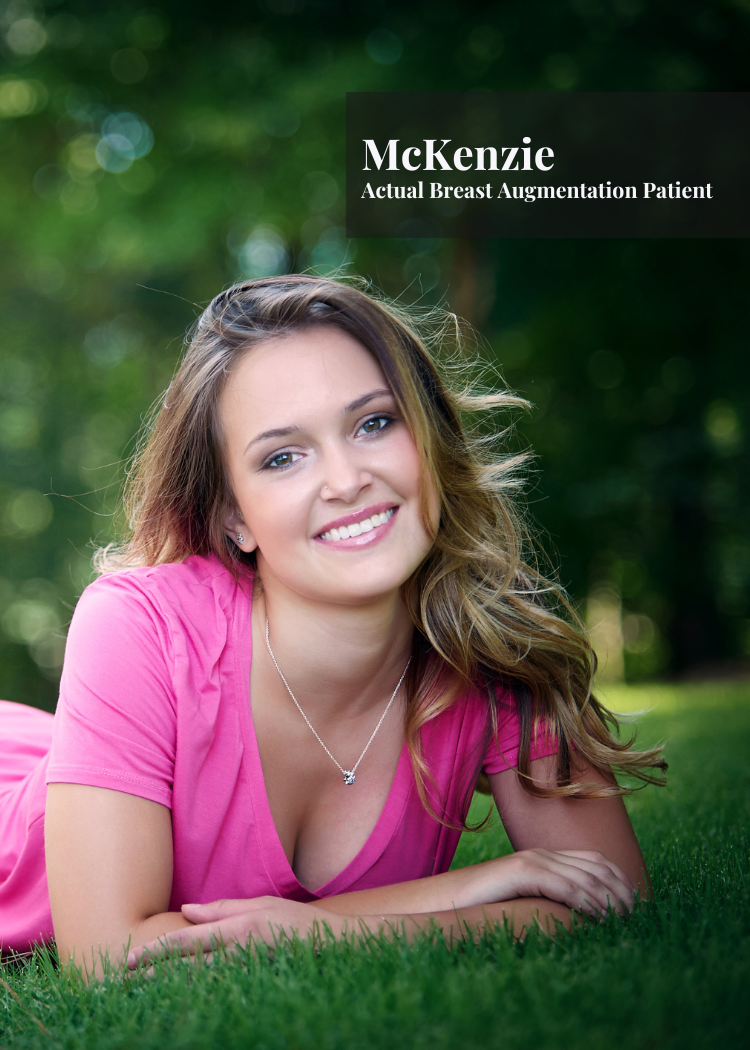 A woman lying on grass outdoors, smiling, with a pink shirt, necklace, and wavy hair, in a park with blurred trees in the background.