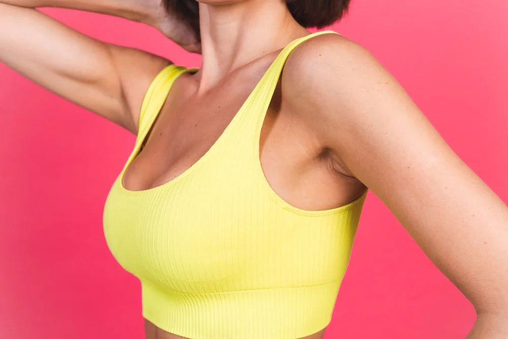 Part of a woman's upper body, wearing a yellow sports bra, against a pink background.