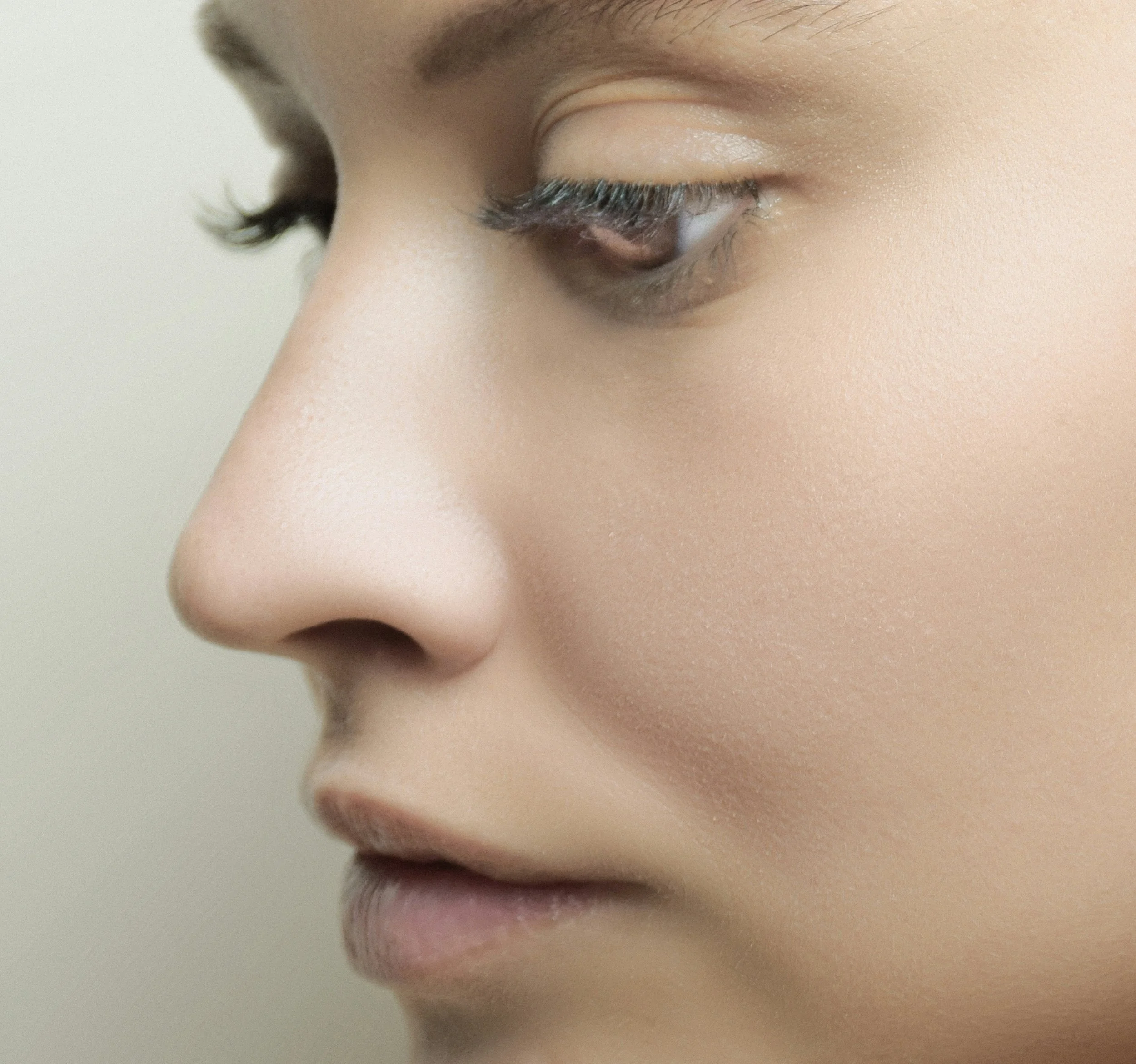 Close-up of a person's closed eye, showcasing eyelashes, eyelid, and eyebrow, with smooth skin.