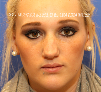 Close-up of a woman with blonde hair, brown eyes, pearl earrings, and a lip piercing, looking directly at the camera with a serious expression.