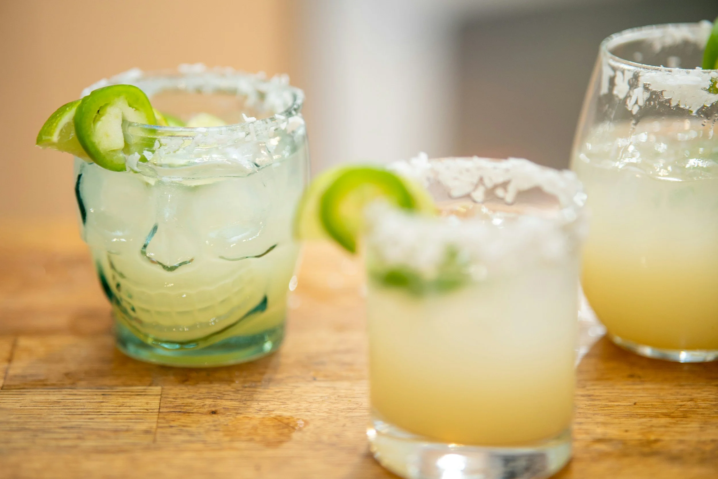 Three glasses of margarita cocktails with lime wedges on a wooden surface.