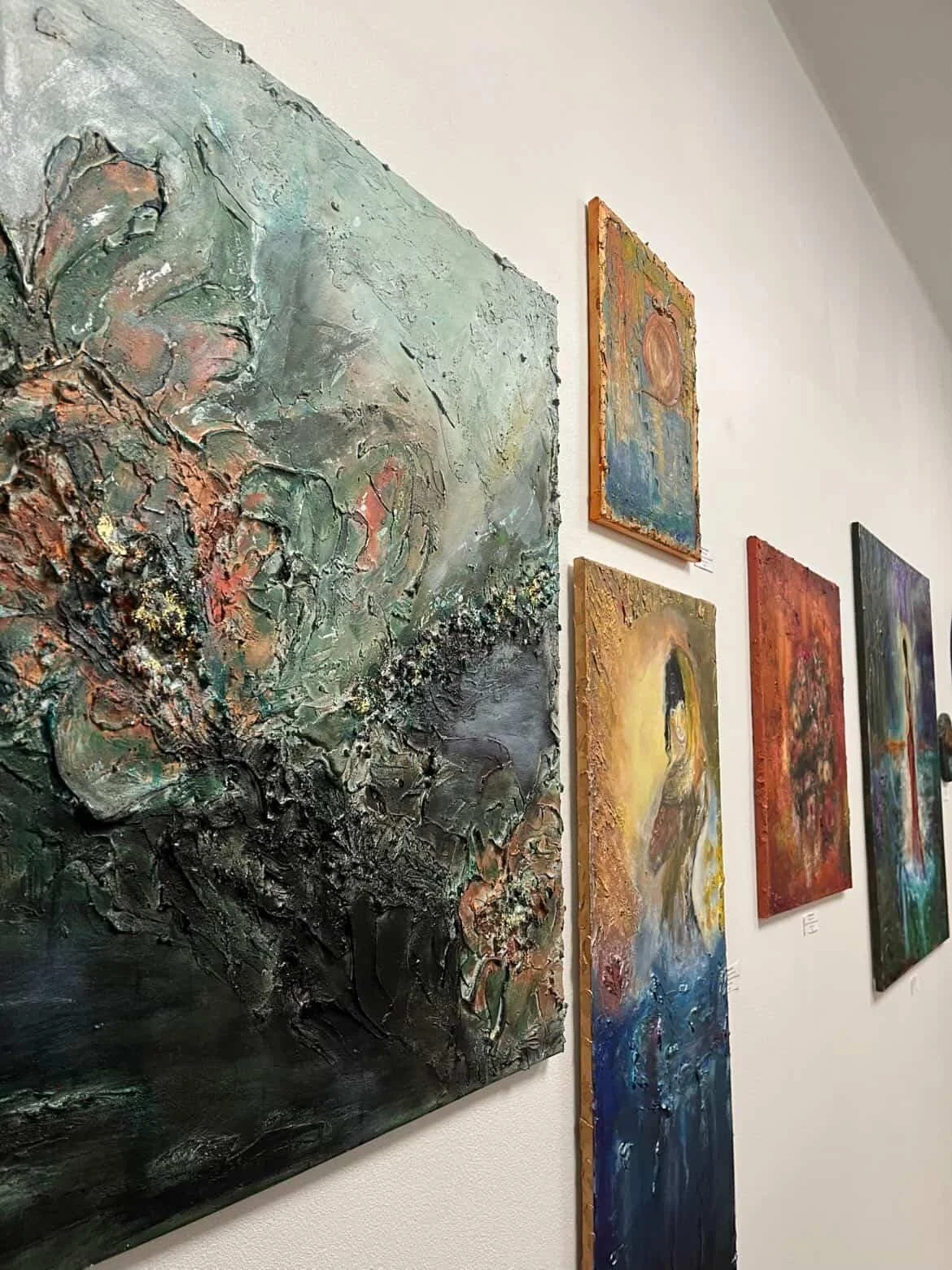 Taidegallerian seinällä on useita abstrakteja maalauksia, joiden värit vaihtelevat vihreästä, siniseen, kultaiseen ja punaiseen. Abstract paintings on the wall. Gallery wall. Artwork. Akryylimaalaus tauluja.