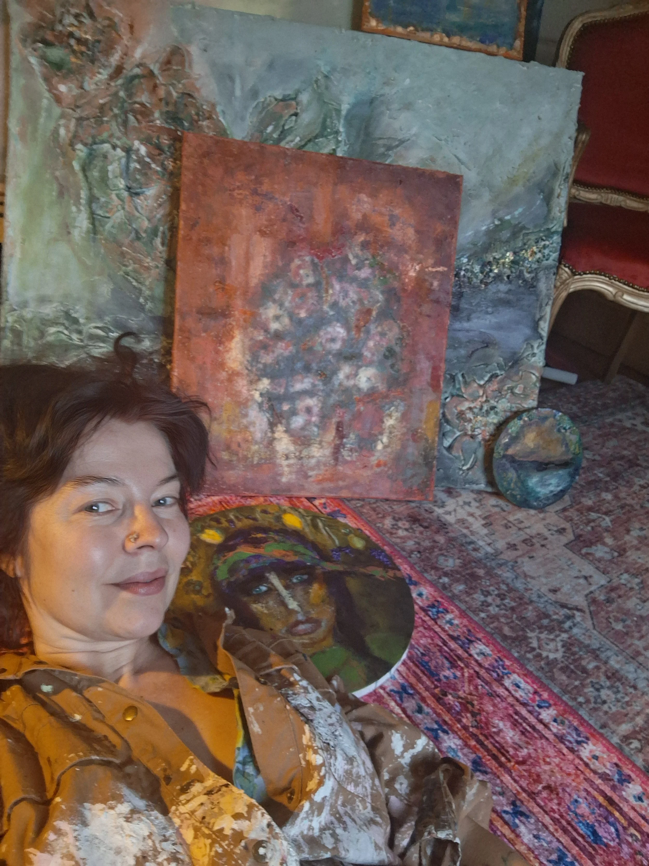 Taiteilija maalaa, taustalla akryylimaalauksia.  Artist is painting with her acrylic paintings.
