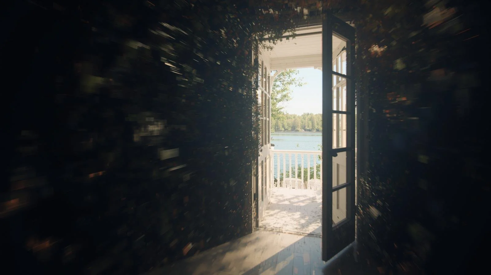 Open door leading to a balcony with a view of a lake and trees, sunny day.