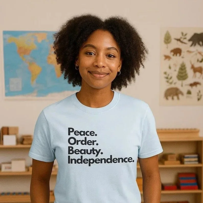 A young woman with curly hair stands indoors, wearing a light blue T-shirt with the words 'Peace. Order. Beauty. Independence.' printed on it. In the background, there is a world map and a poster of animals and trees.