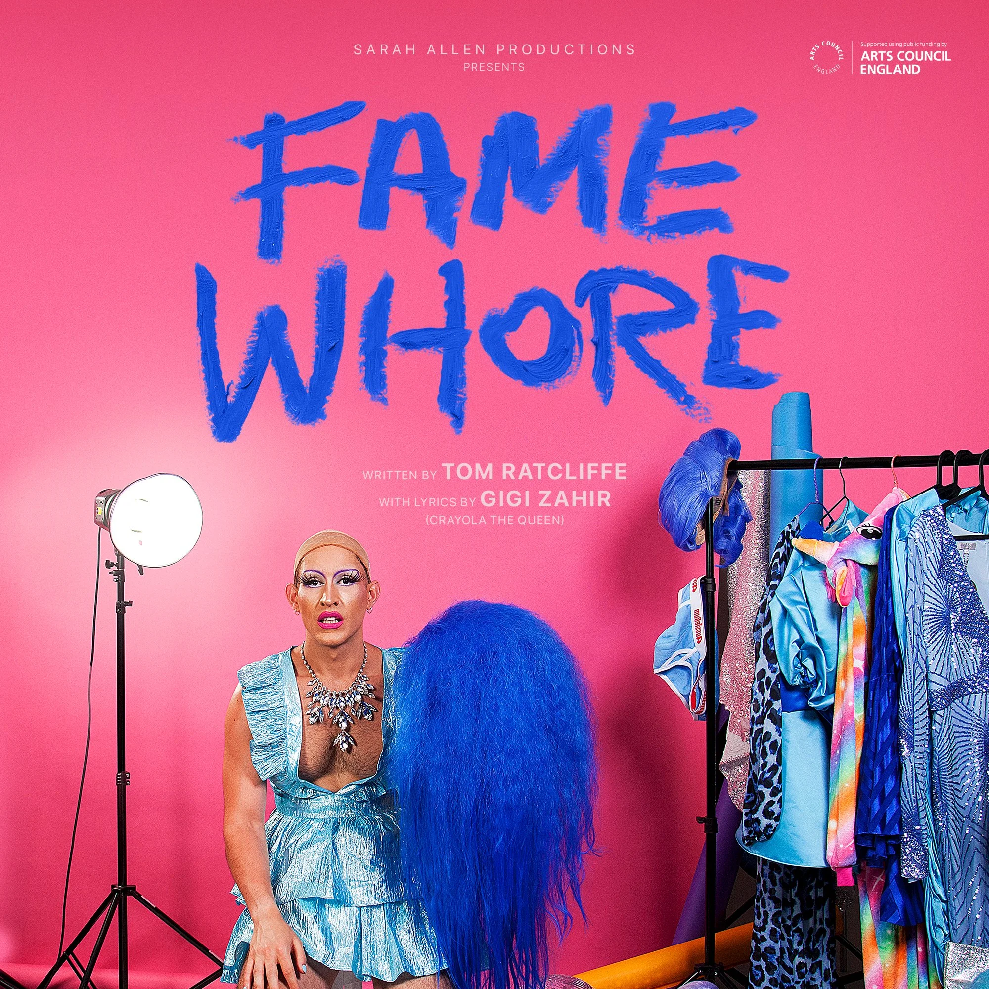 Poster for "Fame Whore," a play by Tom Ratcliffe with lyrics by Gigi Zahir. Features a person in a sparkly blue outfit holding a large blue wig, sitting next to a rack of colorful costumes on a pink background. Text includes 'Sarah Allen Productions' and 'Arts Council England' logos.