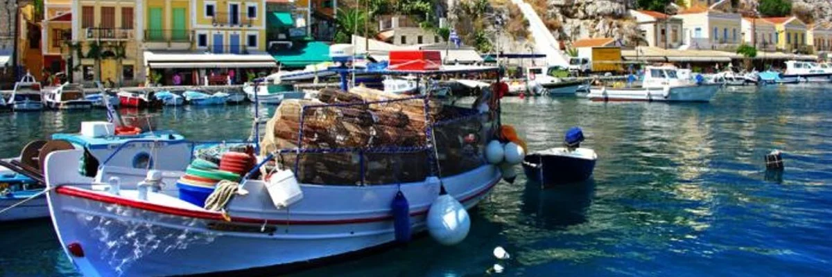 A harbor scene with several boats docked, colorful buildings in the background, and fishing gear on a boat in the foreground.
