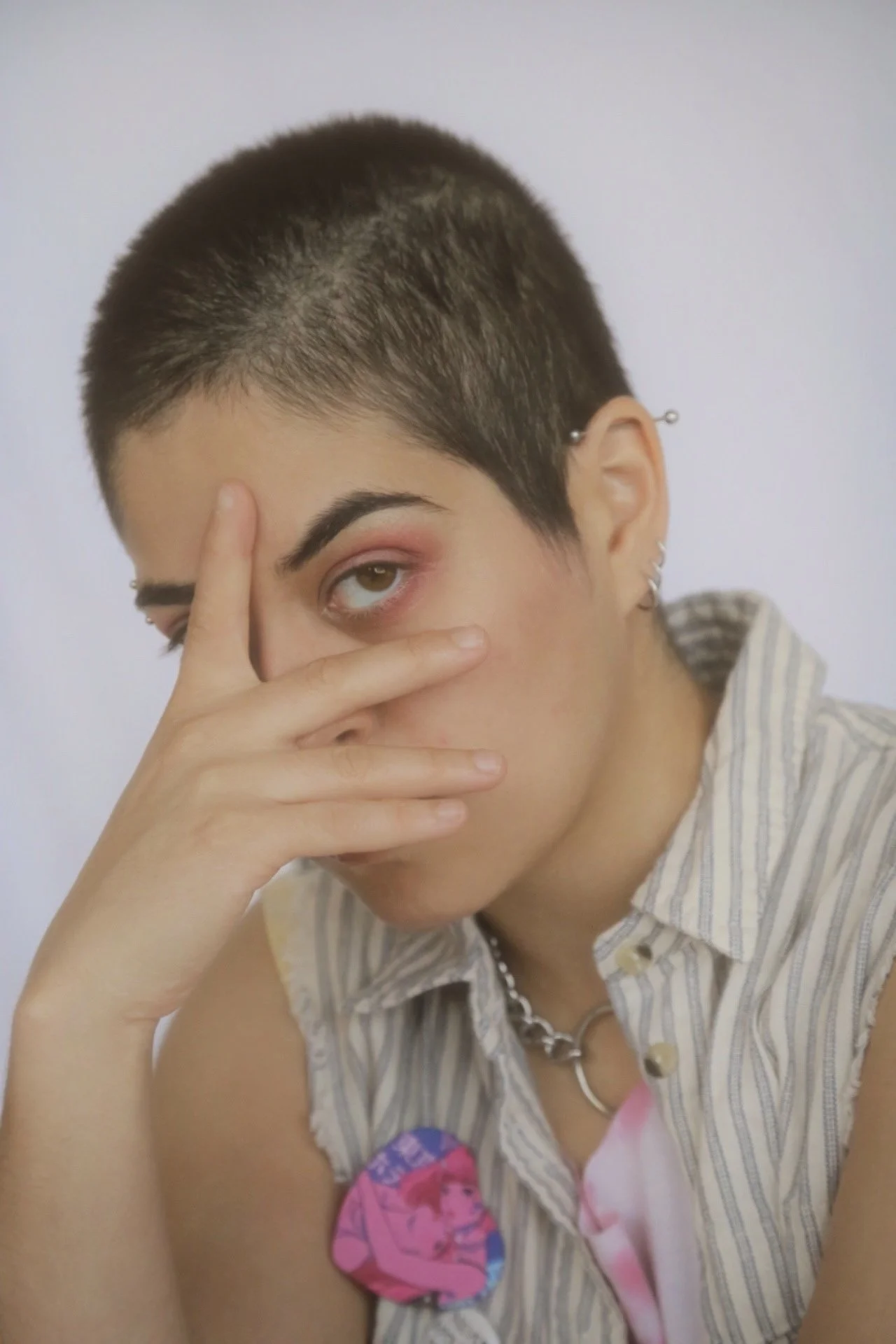 The photo is highlighting an image from the photo series "My Queer Life" which was created to highlight queer people in the city of Chicago. The image showcases a queer person with a shaves head, steel jewelry and pink eye shadow. 