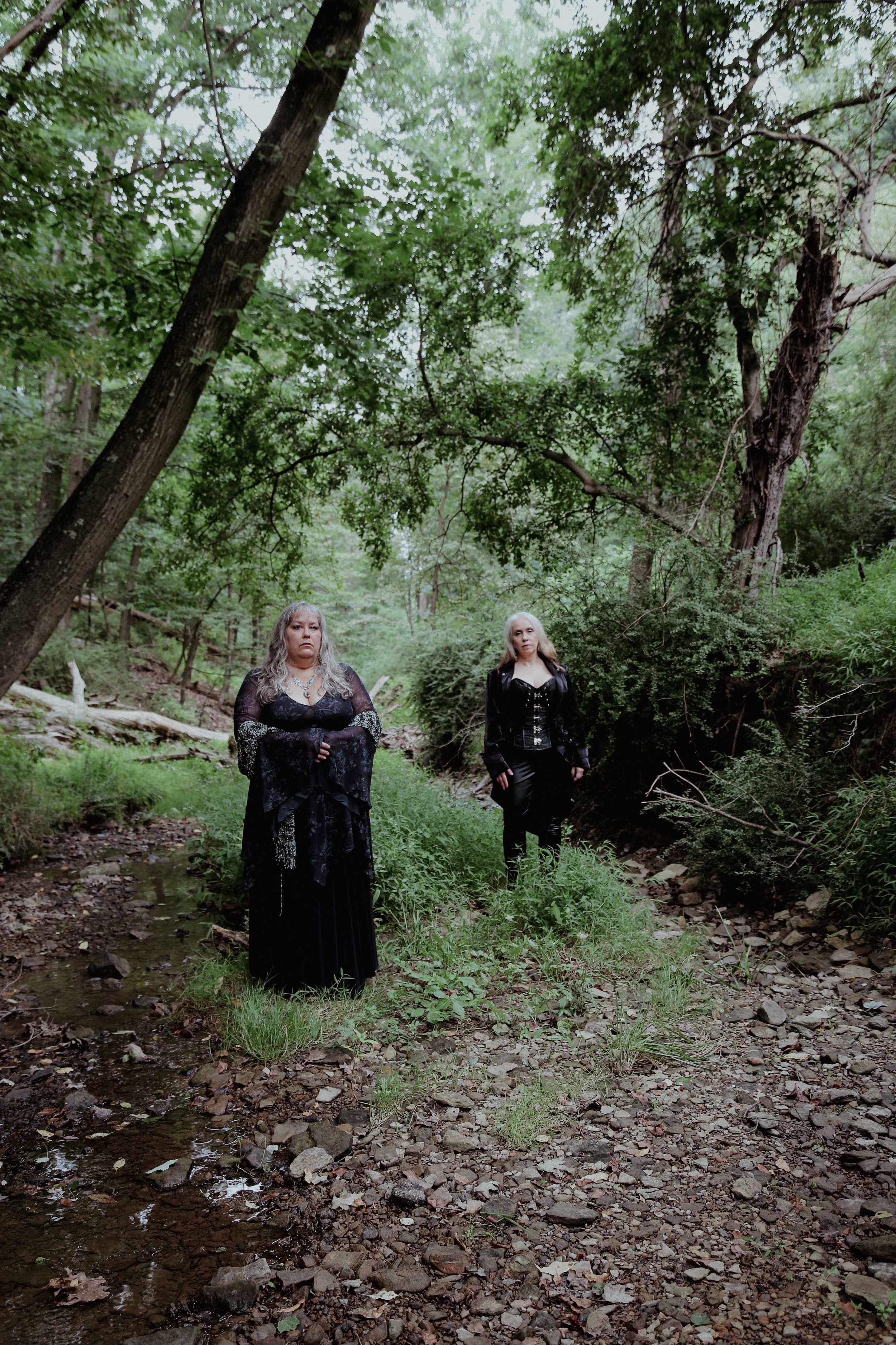 Two women stand in witchy outfits in the forest
