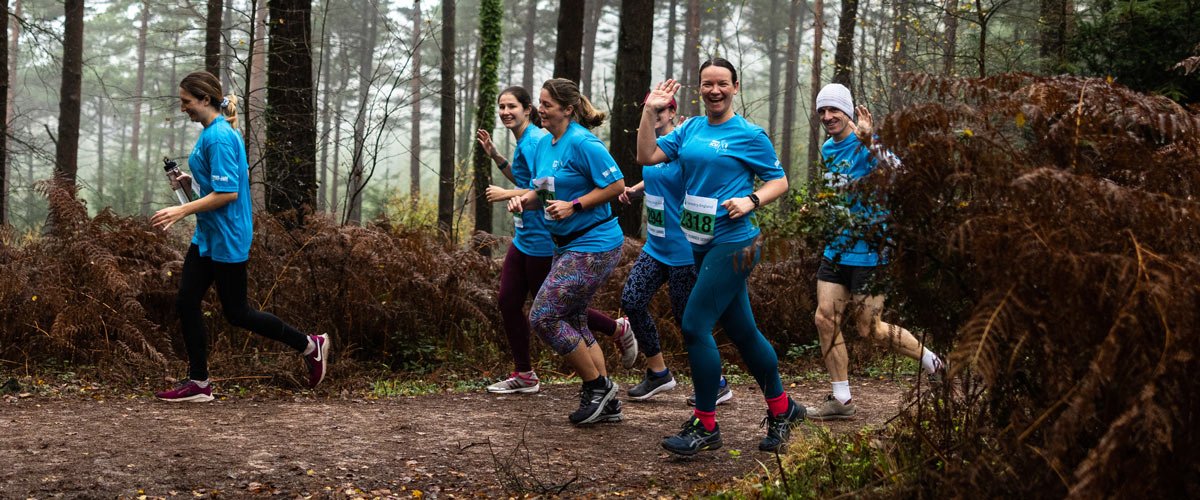 women running in the woods in a friendly pack while they wave at the camera