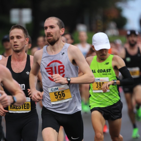 Group of marathon runners in a race, wearing athletic gear and race bibs, running outdoors.