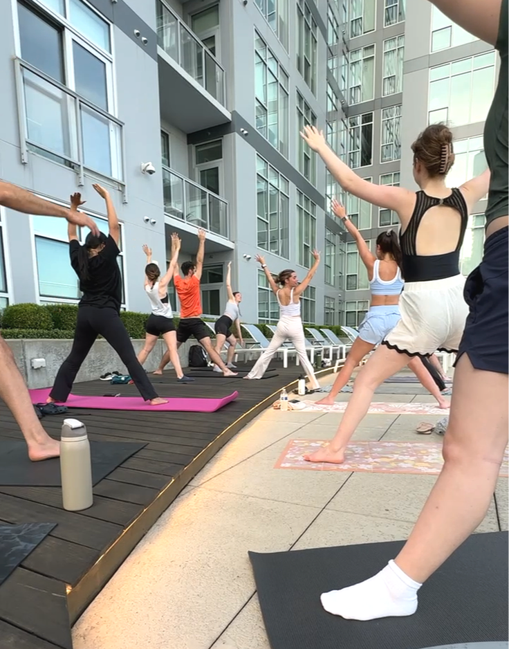 People practicing yoga outdoors on a rooftop terrace with tall modern apartment buildings in the background.