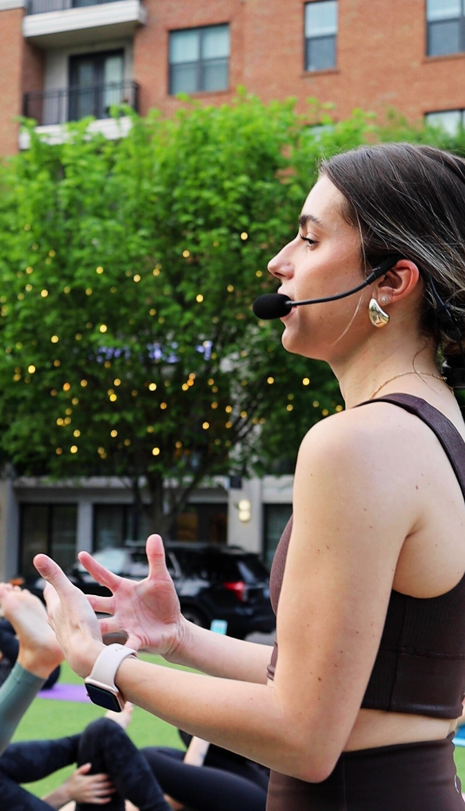 Yoga teacher Daniela Burn wearing a headset teaching an outdoor yoga wellness event.